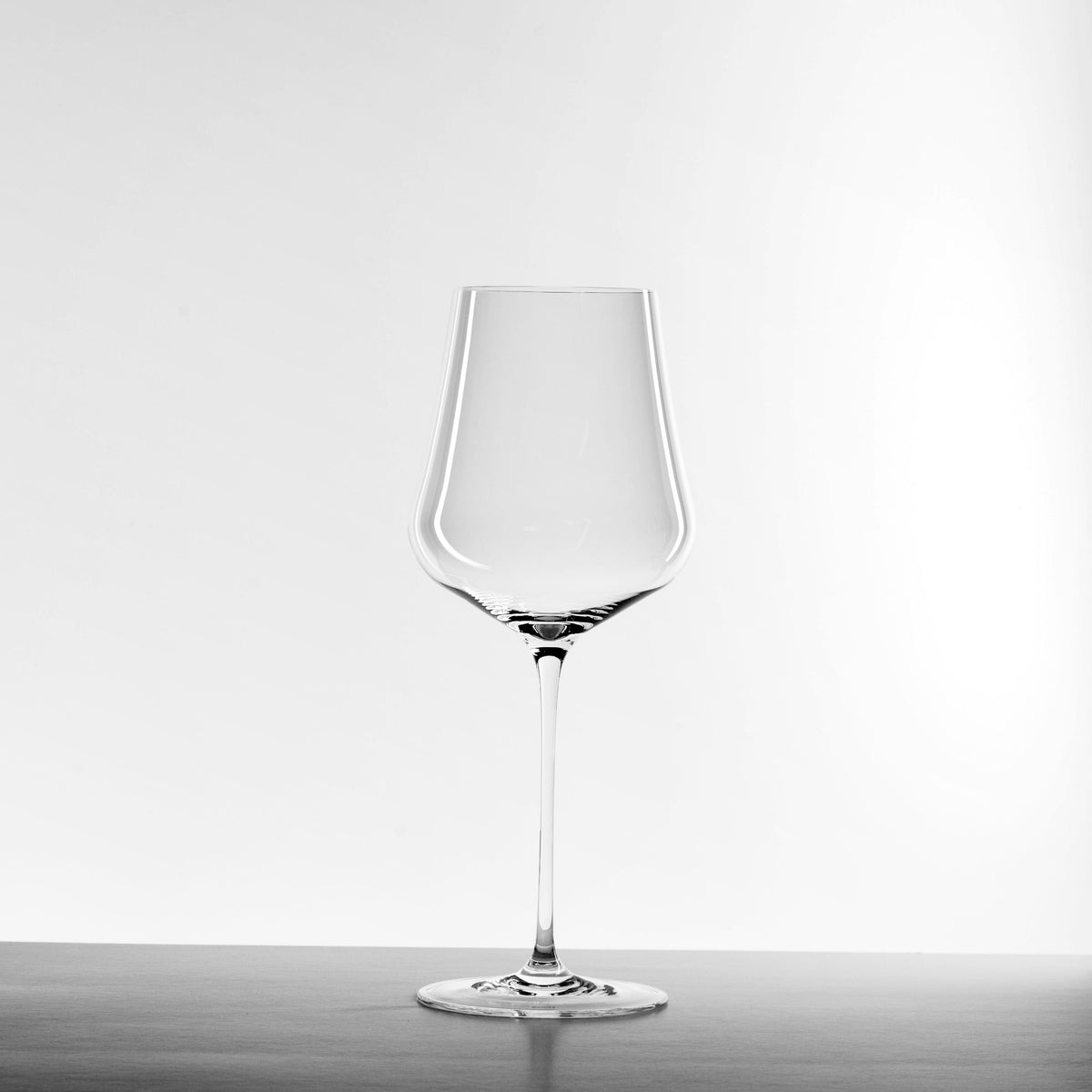 Ein Gabriel Glas Gold Weinglas aus dem exklusiven Set für höchsten Weingenuss steht mit langem Stiel auf Holz vor weißem Hintergrund - perfekt für Kenner und Genießer, inkl. speziellem Pflegetuch.