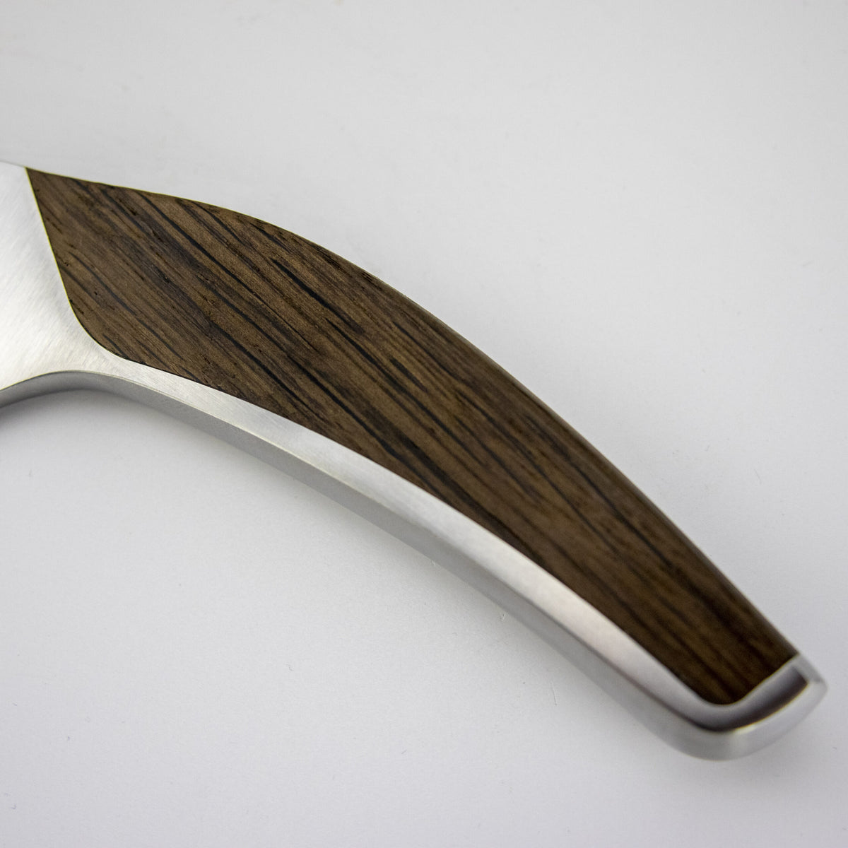 Nahaufnahme des Griffs des Güde Synchros Brotmessers mit 32 cm Klinge. Das schlanke, moderne Design mit einem Griff aus dunklem Holz, eingebettet in einen Korpus aus Edelstahl, zeigt sich perfekt und passt perfekt zu jedem 34 x 21 cm großen Fassholzbrett.