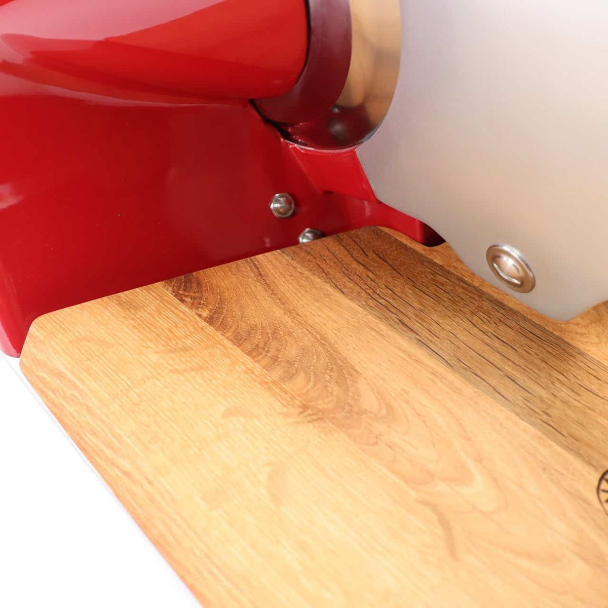 Ein Detailfoto zeigt das Palatina-Werkstatt Einlegebrett passend für Berkel Home Line 250, ein hölzernes Schneidebrett, das fest an einem leuchtend roten Küchengerät aus Metall befestigt ist. Das Brett zeigt seine natürliche Holzmaserung, ergänzt durch die teilweise sichtbaren glänzenden Metallkomponenten des Allesschneiders Berkel Home Line 250.