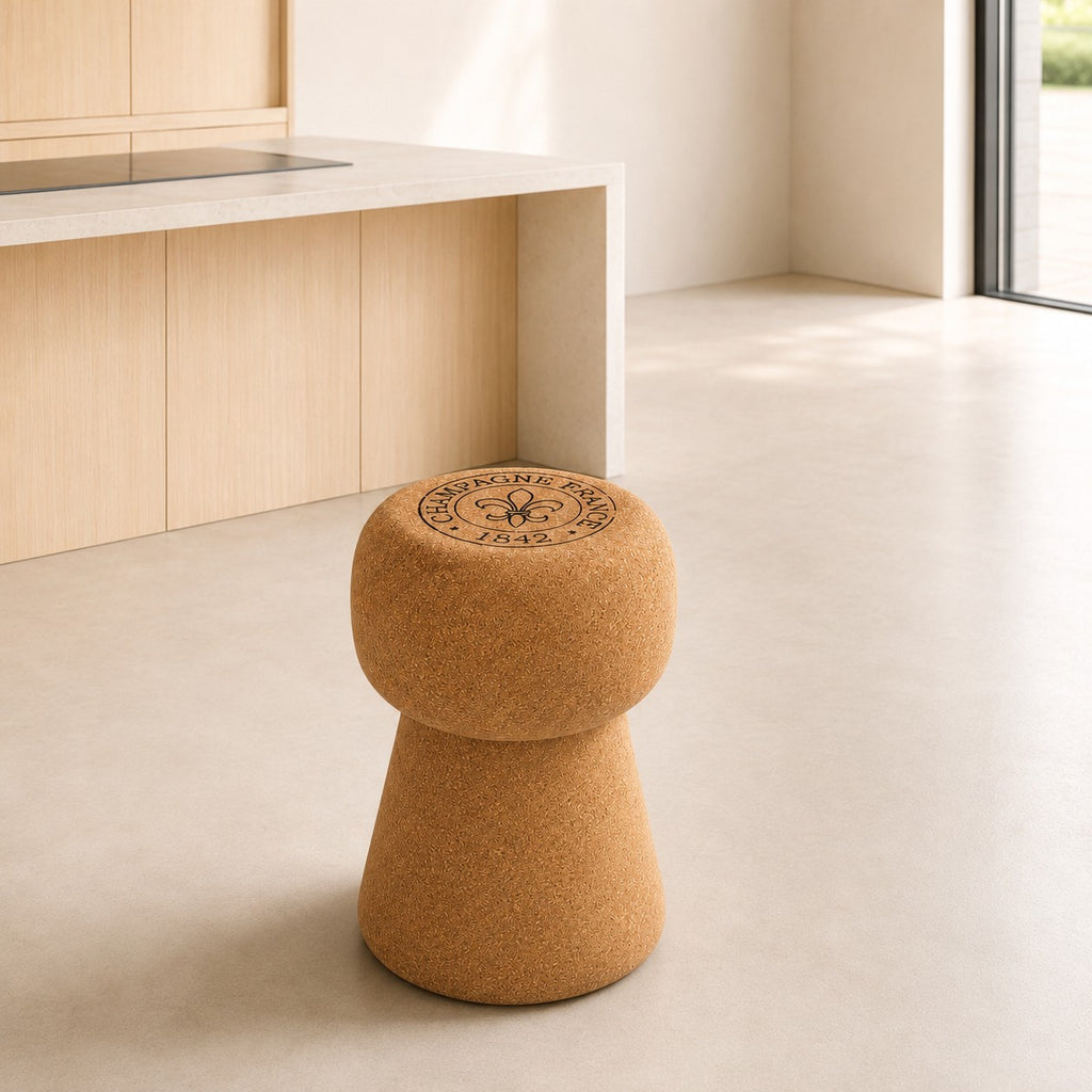Ein hochwertiger Hocker aus Kork in Form eines Champagnerkorkens steht in einer modernen, minimalistisch eingerichteten Küche mit hellen Holzschränken und weichem, natürlichem Licht.