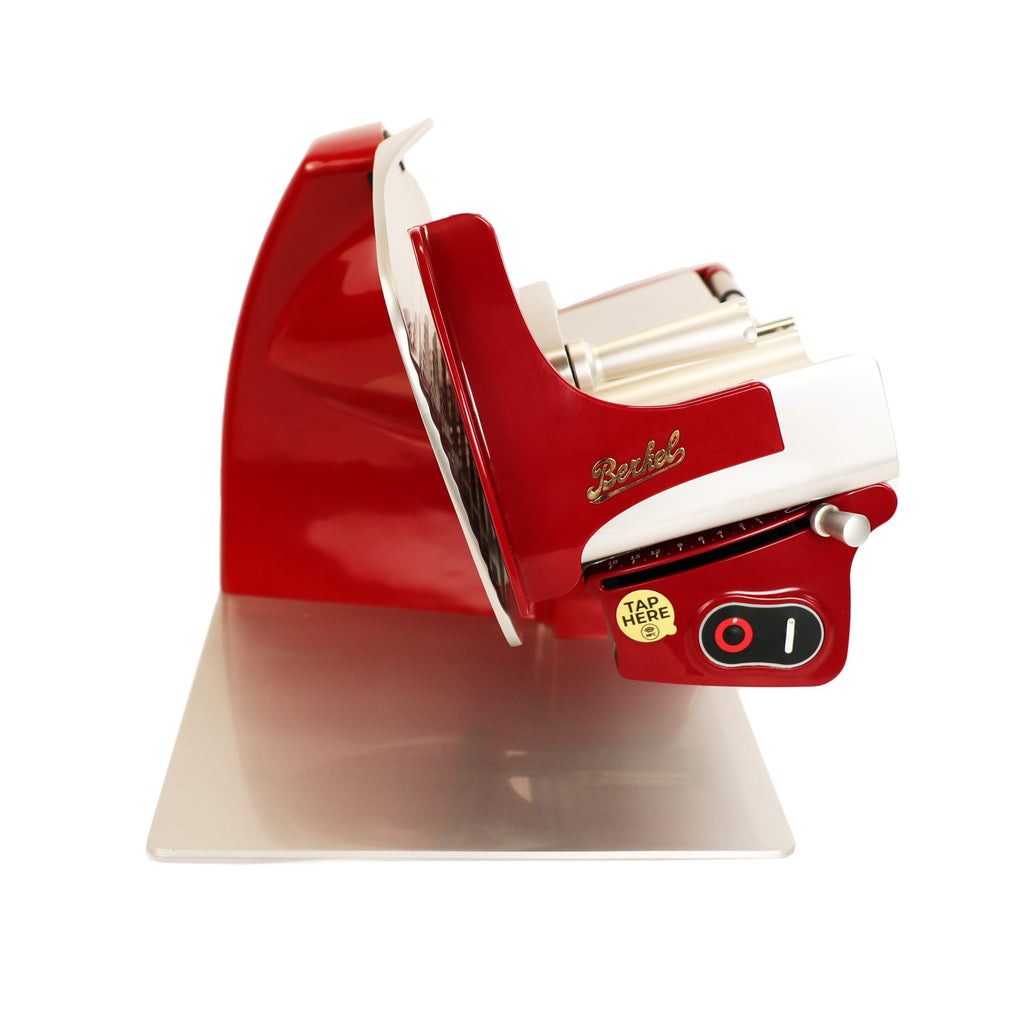 Die Berkel Home Line 200 Plus rot - Aufschnittmaschine mit Wellenschliff-Bausatz für Brot besitzt eine glänzende Metallklinge, einen schwarzen Schalter und einen gelben "TAP HERE"-Sticker auf einer flachen Metallbasis.