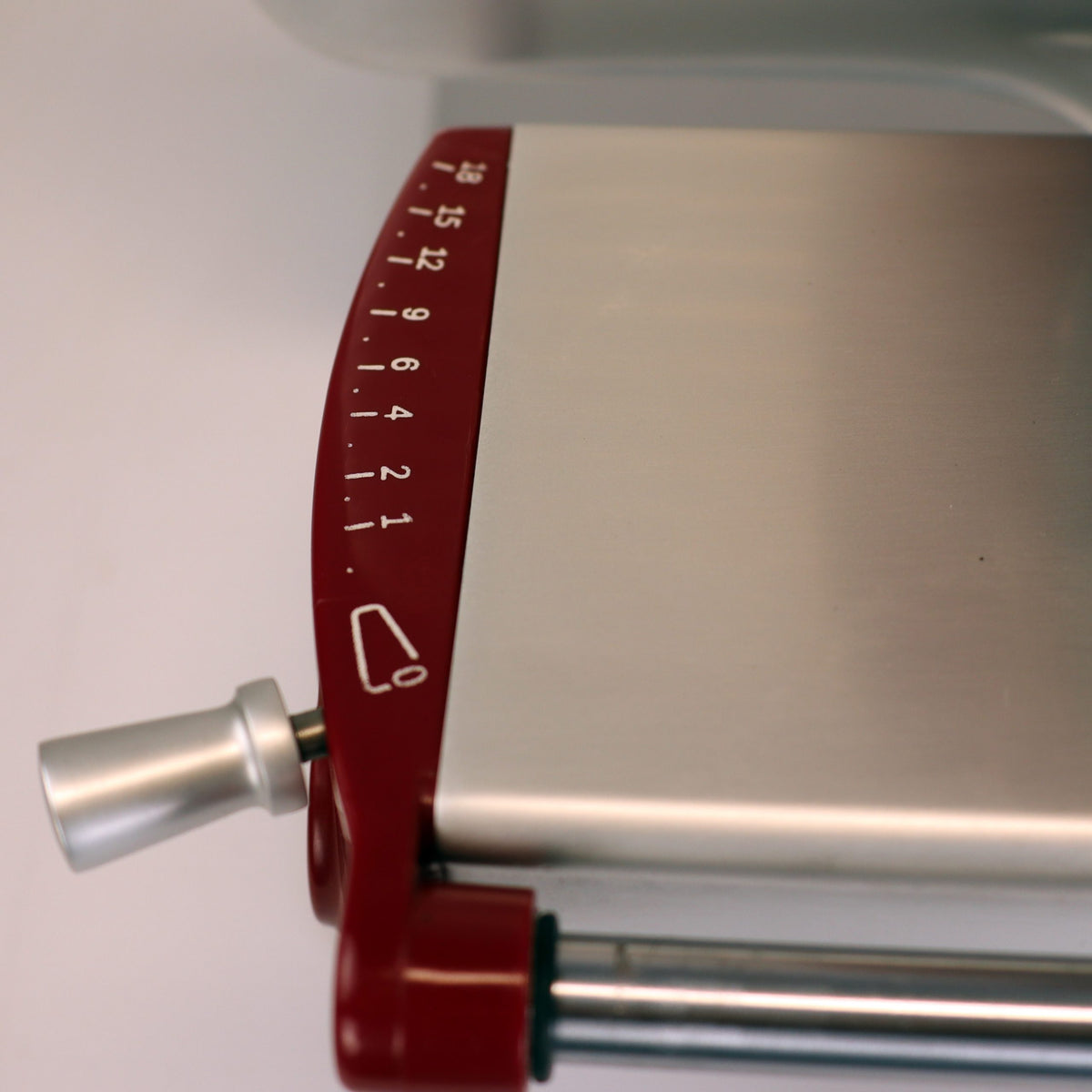 Eine Nahaufnahme der Berkel Home Line 200 Plus rot Aufschnittmaschine, einem neuen Modell mit rotem Drehknopf (1-15), silbernem Griff links sowie handgefertigtem Unikat-Schneidebrett & Wellenschliff-Bausatz für Brot.