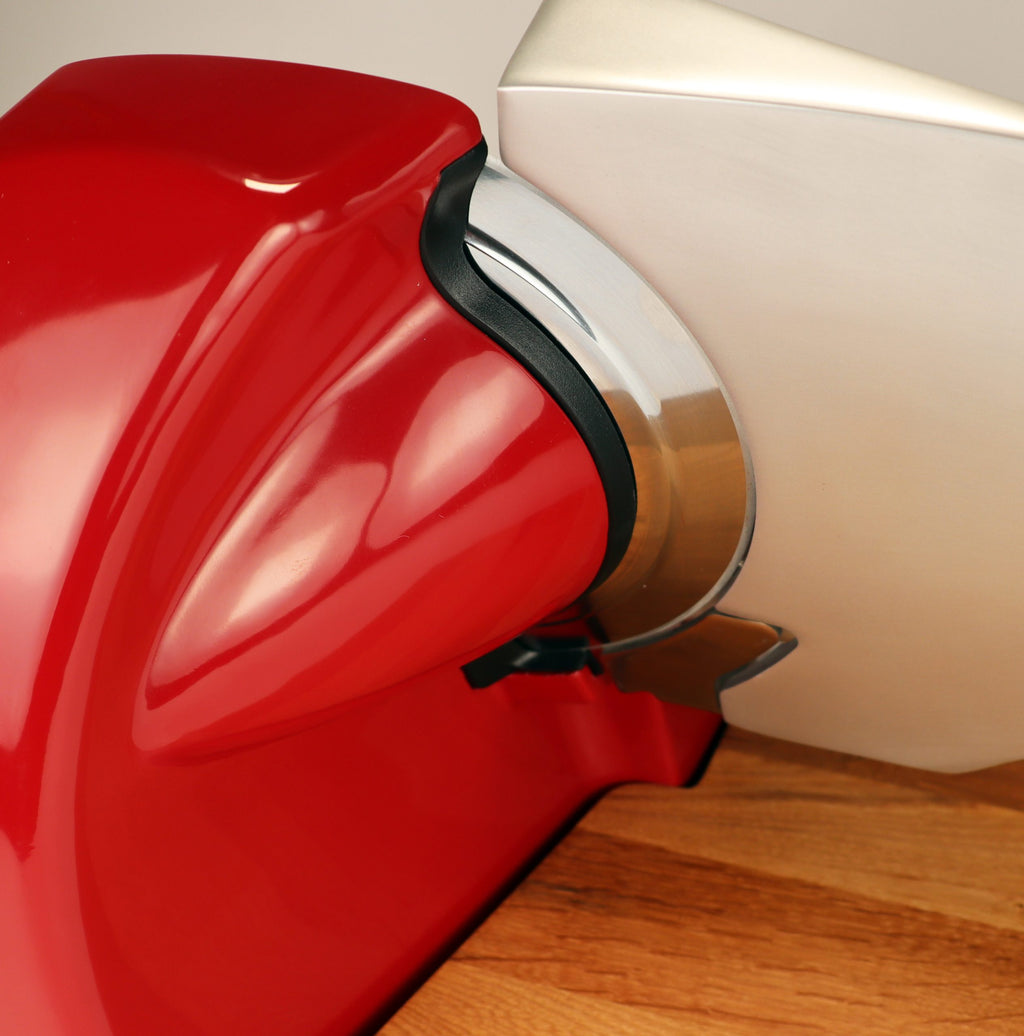 Nahaufnahme der Berkel Home Line 200 Plus rot Aufschnittmaschine, einem neuen Modell mit einem einzigartigen handgefertigten Schneidebrett und Wellenschliff-Kit für Brot, das sein schlankes, geschwungenes Design und die detaillierte Klinge auf einer Holzoberfläche zeigt.