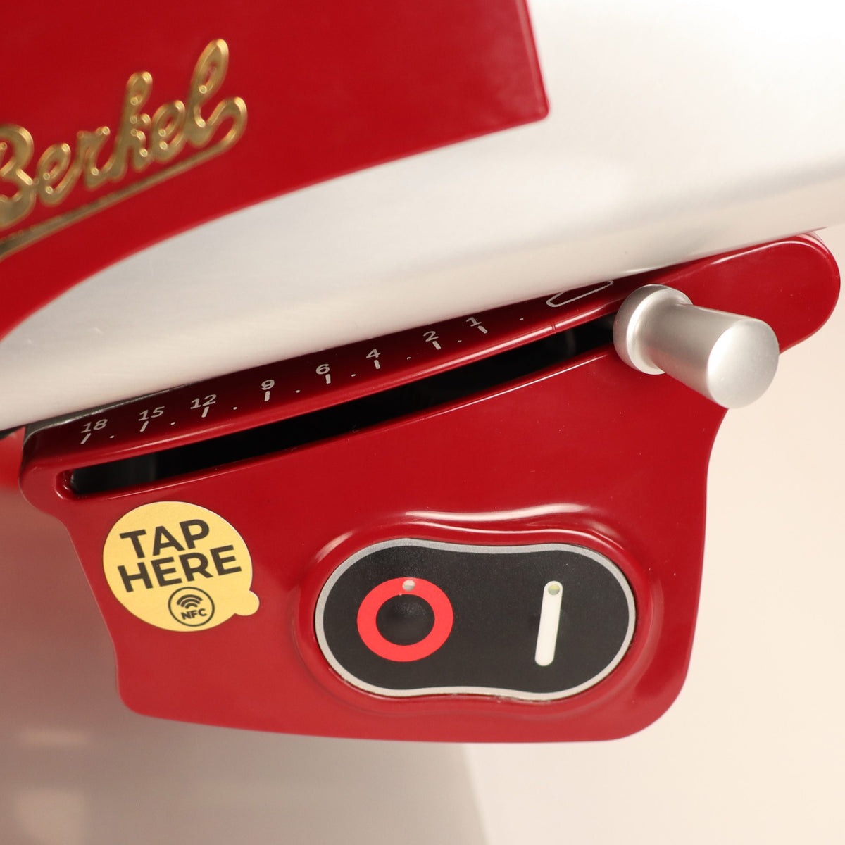 Nahaufnahme der Berkel Home Line 200 Plus rot Aufschnittmaschine (neues Modell) mit einzigartigem handgefertigtem Schneidebrett, Brotwellenzackensatz, Dickeneinstellknopf, NFC-Aufkleber "TAP HERE" und einem Teil des goldenen Markenlogos.