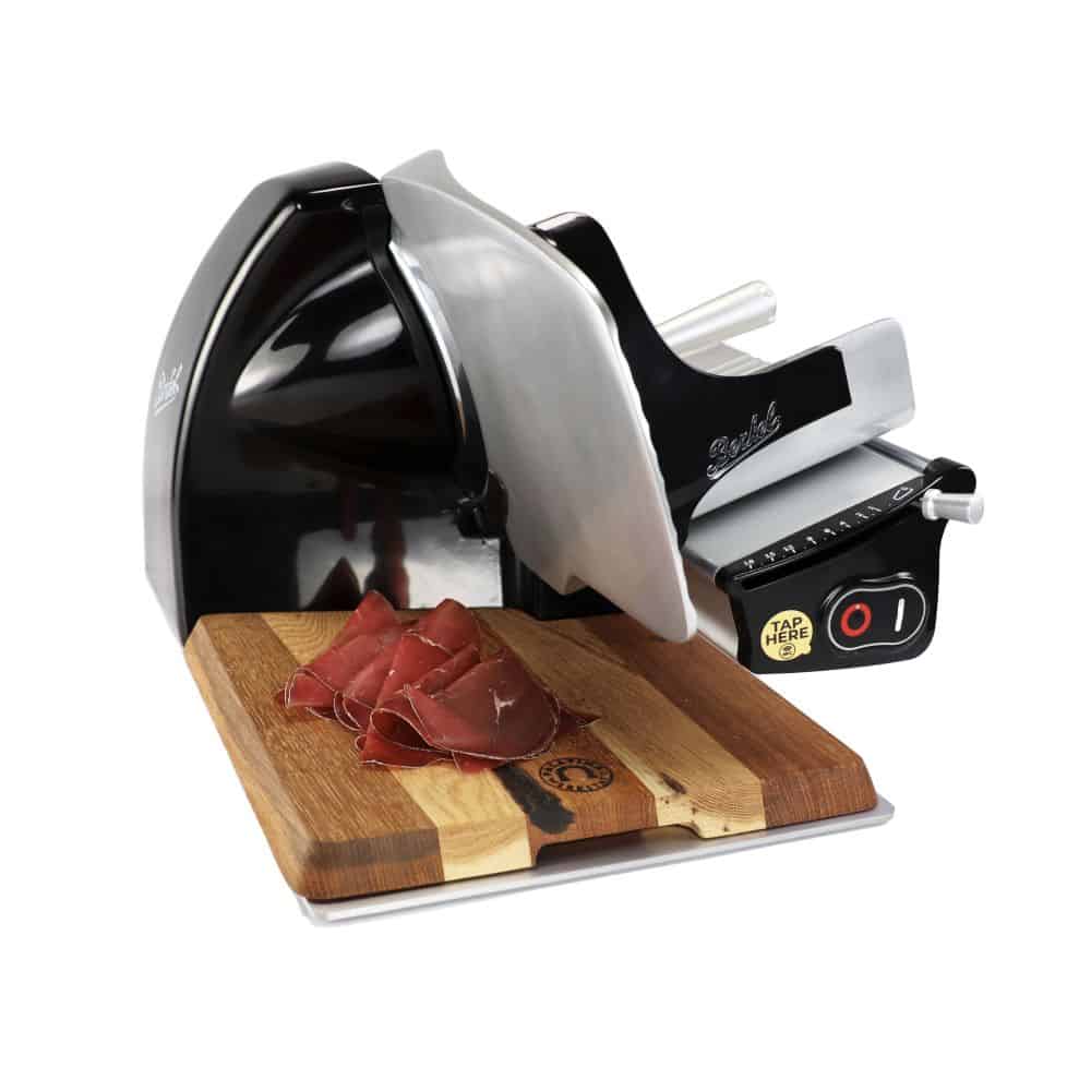 Eine elegante Berkel Home Line 200 Plus Schwarz Aufschnittmaschine - Neues Modell - Schneidemaschine auf weißem Hintergrund, mit ein paar Scheiben Wurst auf einem einzigartigen, 100 % handgefertigten Holzschneidebrett davor. Die Maschine verfügt über ein rundes Messer und einen Bedienknopf an der Seite.