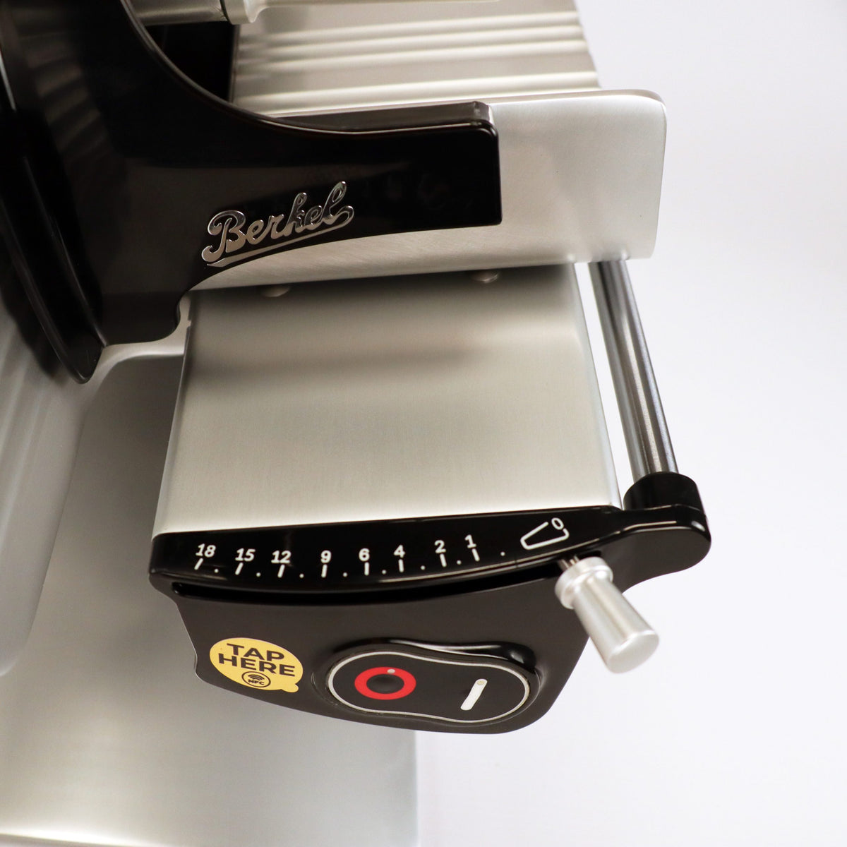 Nahaufnahme der Berkel Home Line 200 Plus schwarz - Aufschnittmaschine, neues Modell, mit nummeriertem Dickenregler, Hebel, Power-Taste und "TAP HERE"-Sticker auf der schwarzen Metalloberfläche, inkl. Unikat-Schneidebrett & Wellenschliff-Bausatz für Brot.