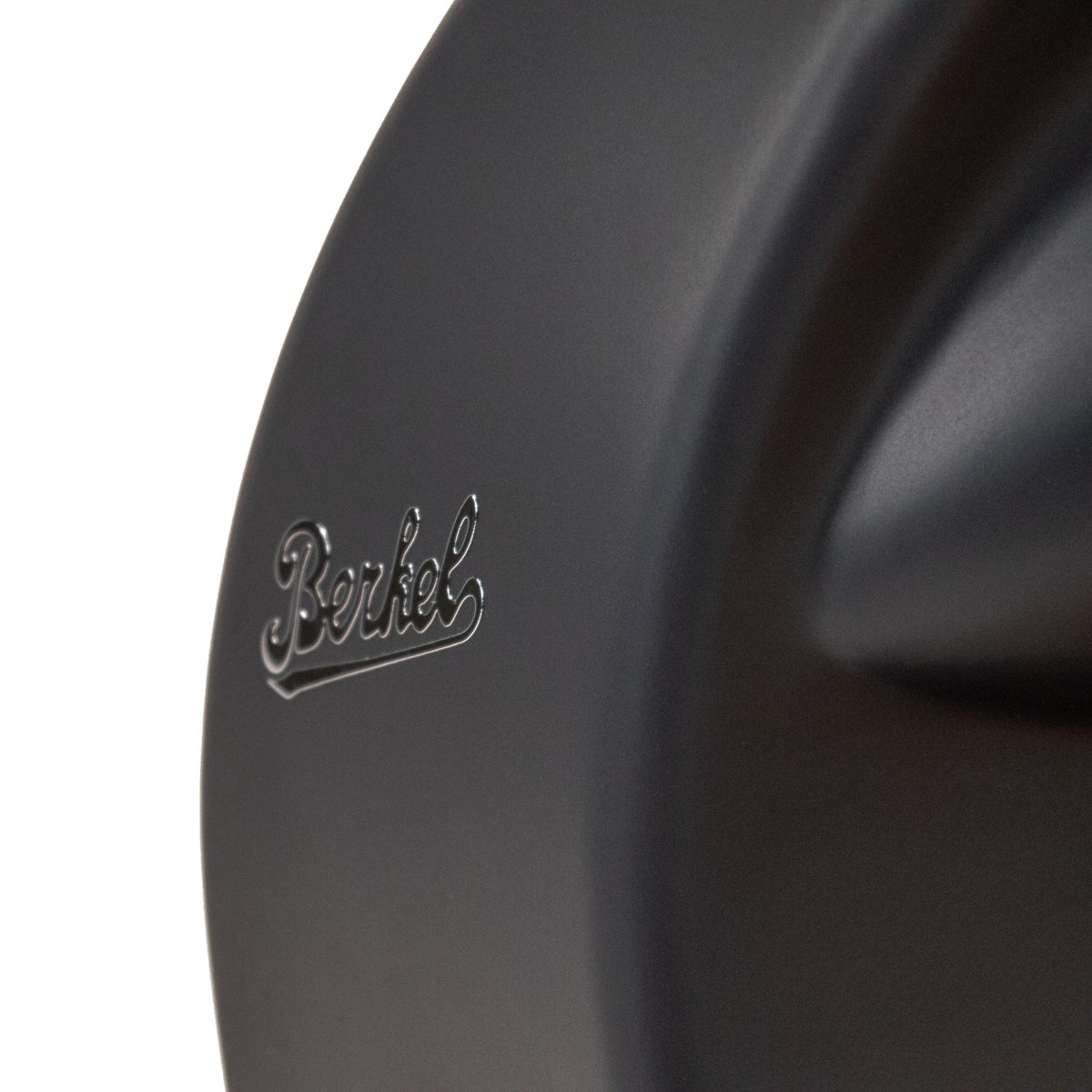 Nahaufnahme der mattschwarzen Berkel Home Line 200 Plus mit dem Schriftzug "Berkel" in glänzender Schrift. Die Beleuchtung hebt die geschwungene Oberfläche hervor, die die handwerkliche Qualität der exklusiven Schneidemaschine und das einzigartige Brotschneidezubehör mit handgefertigtem Brett widerspiegelt.