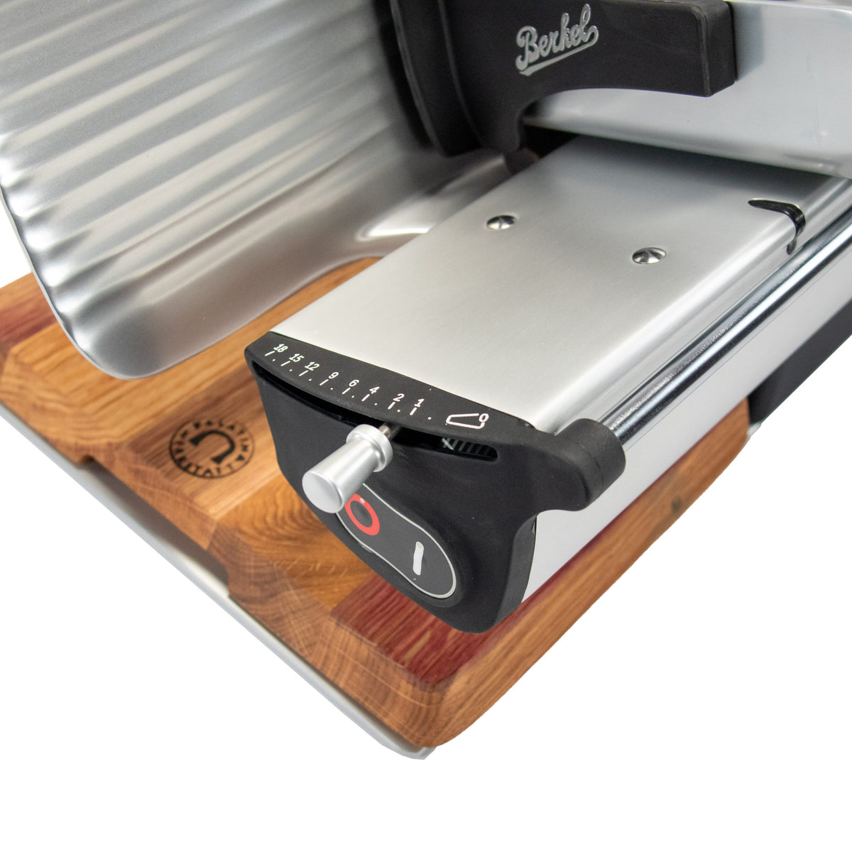 Nahaufnahme der Berkel Home Line 200 Plus schwarz matt Aufschnittmaschine mit handgefertigtem Schneidebrett & Wellenschliff-Bausatz für Brot auf Holz, mit sichtbarem Einstellknopf, nummeriertem Drehregler und Berkel-Logo.