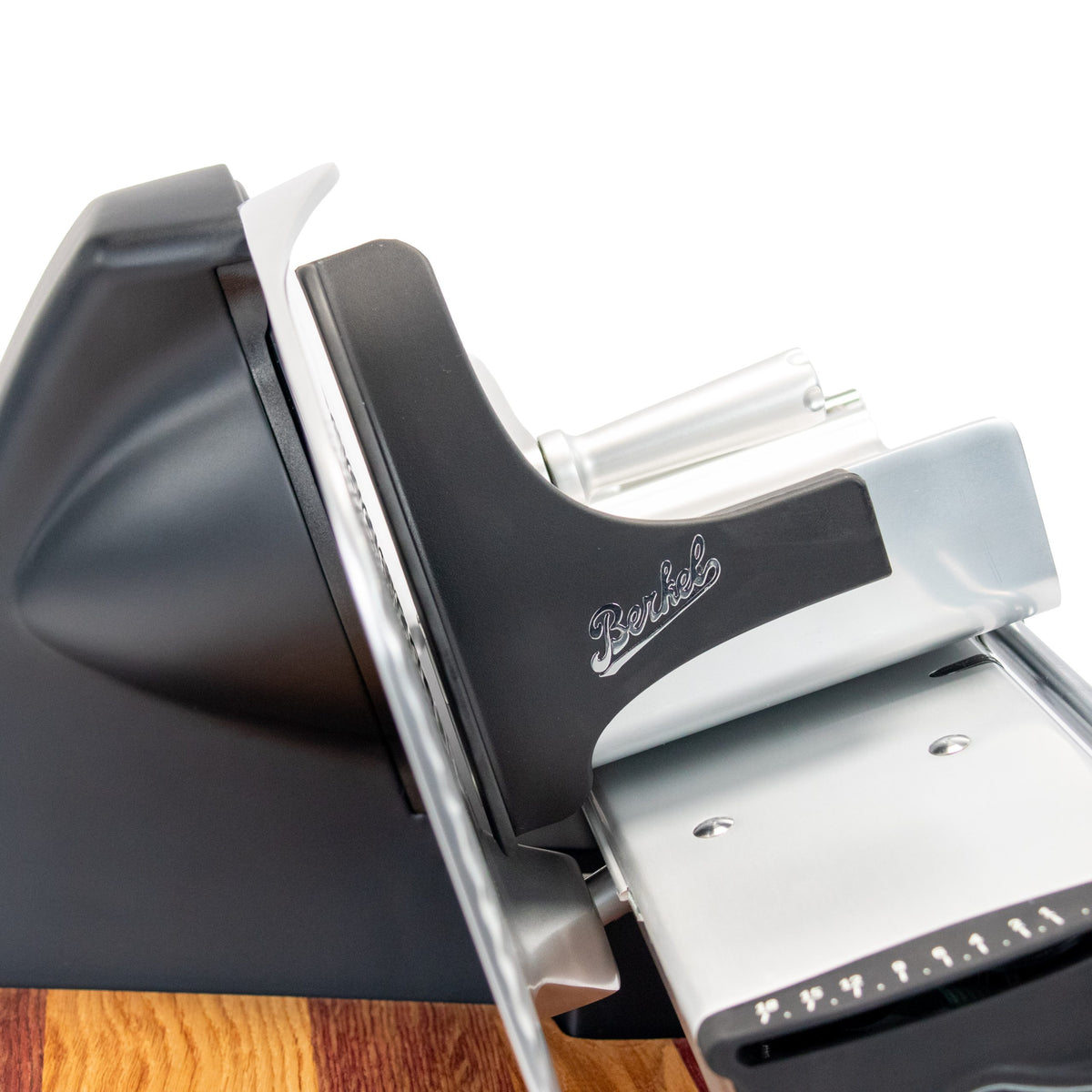 Eine Seitenansicht der Berkel Home Line 200 Plus schwarz matt Aufschnittmaschine, dem neuen Modell mit handgefertigtem, einzigartigem Schneidebrett und Brotwellenschneidsatz, das auf einer Holzoberfläche ruht.
