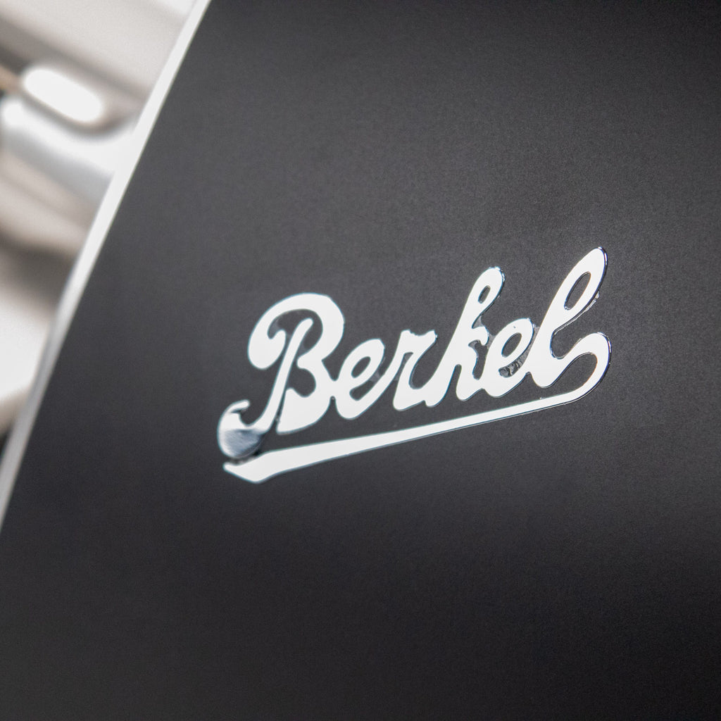 Nahaufnahme des glänzenden "Berkel"-Logos in Schreibschrift auf der glatten, dunklen Oberfläche der Berkel Home Line 250 Plus Schwarz MATT Aufschnittmaschine - neues Modell mit handgefertigtem Schneidebrett Unikat.
