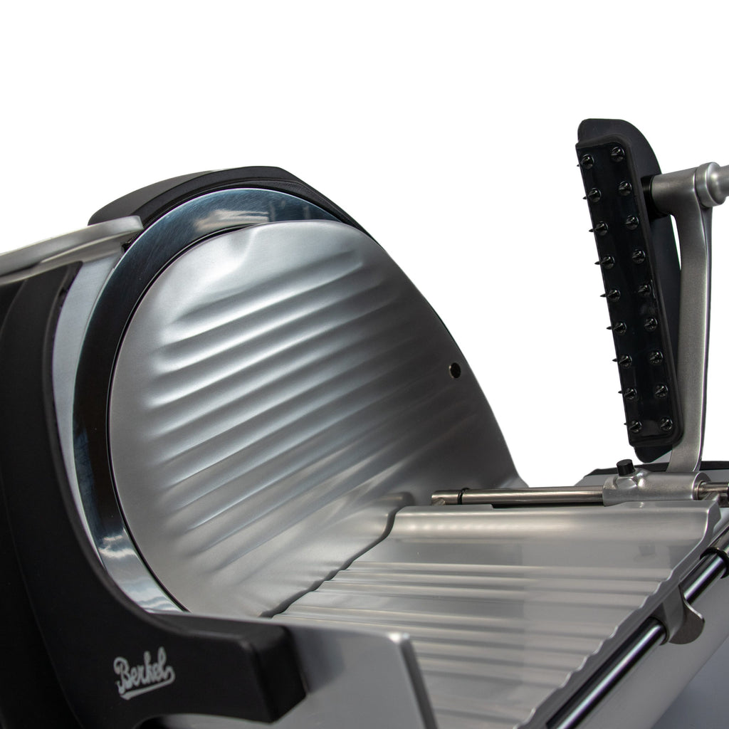 Nahaufnahme der Berkel Home Line 250 Plus Schwarz MATT Aufschnittmaschine - neues Modell - mit rundem Metallmesser, Rillen-Schlitten, schwarzem Griff und Schutz auf weißem Hintergrund, inkl. handgefertigtem Schneidebrett Unikat.