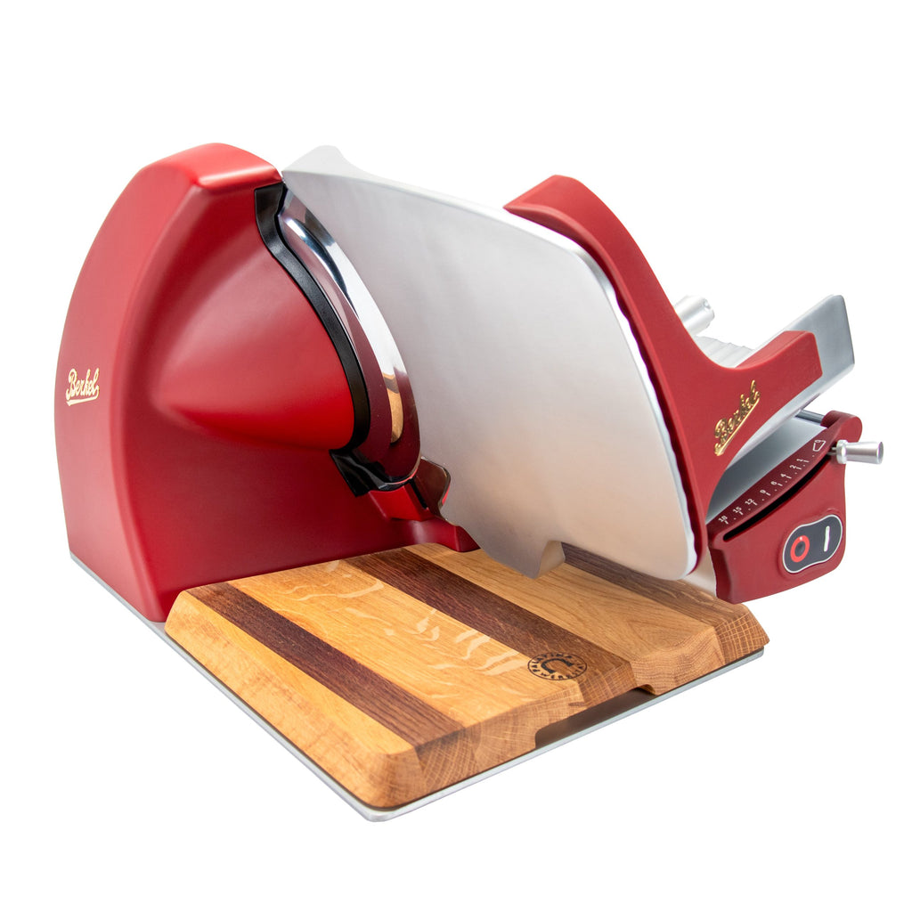 A Berkel Home Line 250 Plus Rot MATT Aufschnittmaschine - Neues Modell - mit Edelstahlklinge steht auf einem 100% handgefertigten Schneidebrett Unikat. Die Maschine bietet Einstellungskontrollen und einen Ein/Aus-Schalter.