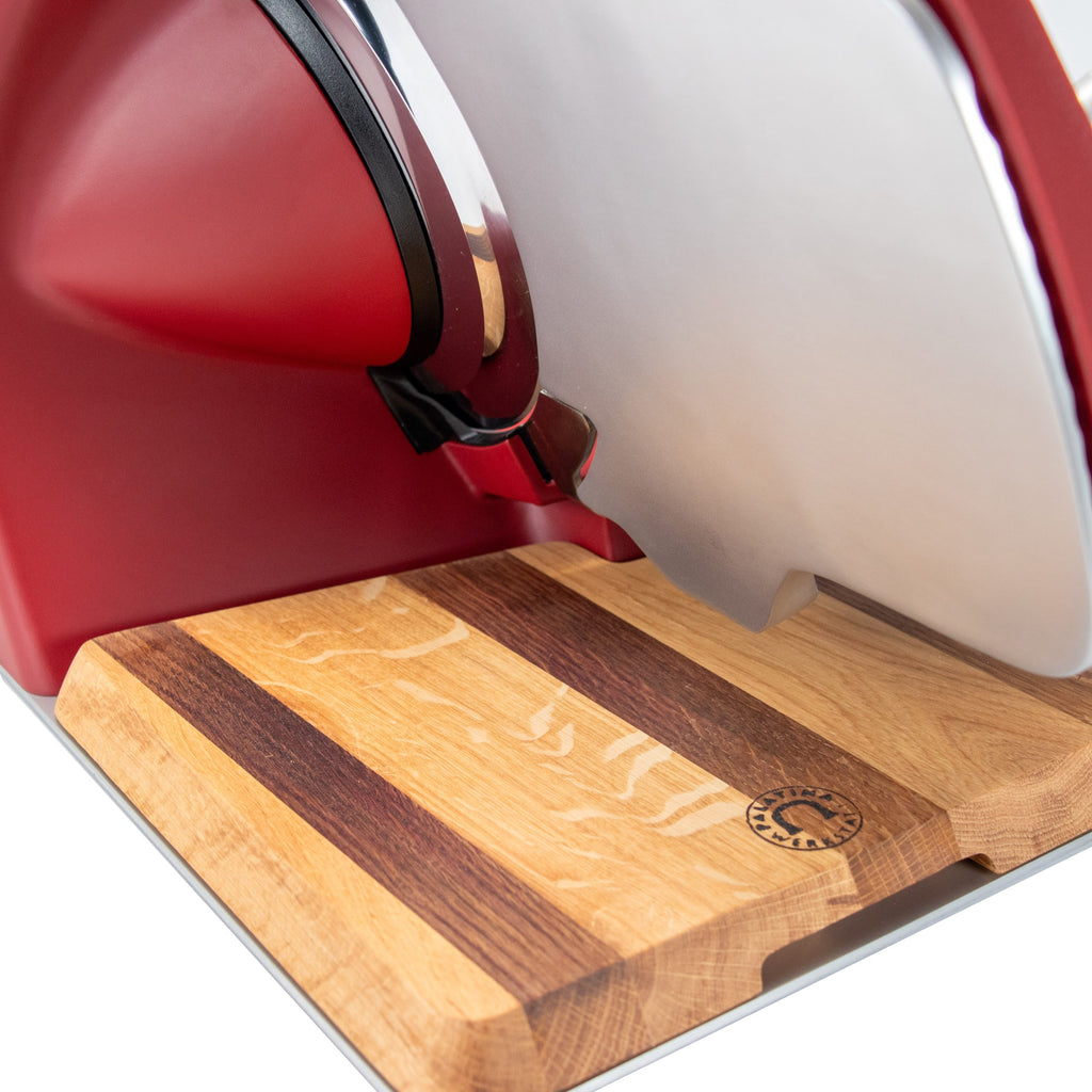 Nahaufnahme der Berkel Home Line 250 Plus Rot MATT Aufschnittmaschine (neues Modell) mit einem einzigartigen, 100% handgefertigten Schneidebrett mit hellen und dunklen Streifen und einem runden Logo in der Ecke.