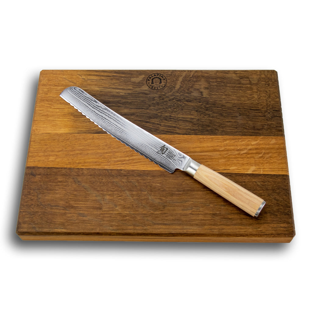 Ein Kai Shun Classic White DM-0705W Wellenschliffmesser mit Holzgriff liegt auf einem rechteckigen, handgefertigten Schneidebrett mit den Maßen 40x30 cm und zweifarbigem Holz. Die 23,0 cm lange Damastklinge weist eine gemusterte Textur auf und das Schneidebrett ist oben in der Mitte mit einem Emblem verziert.