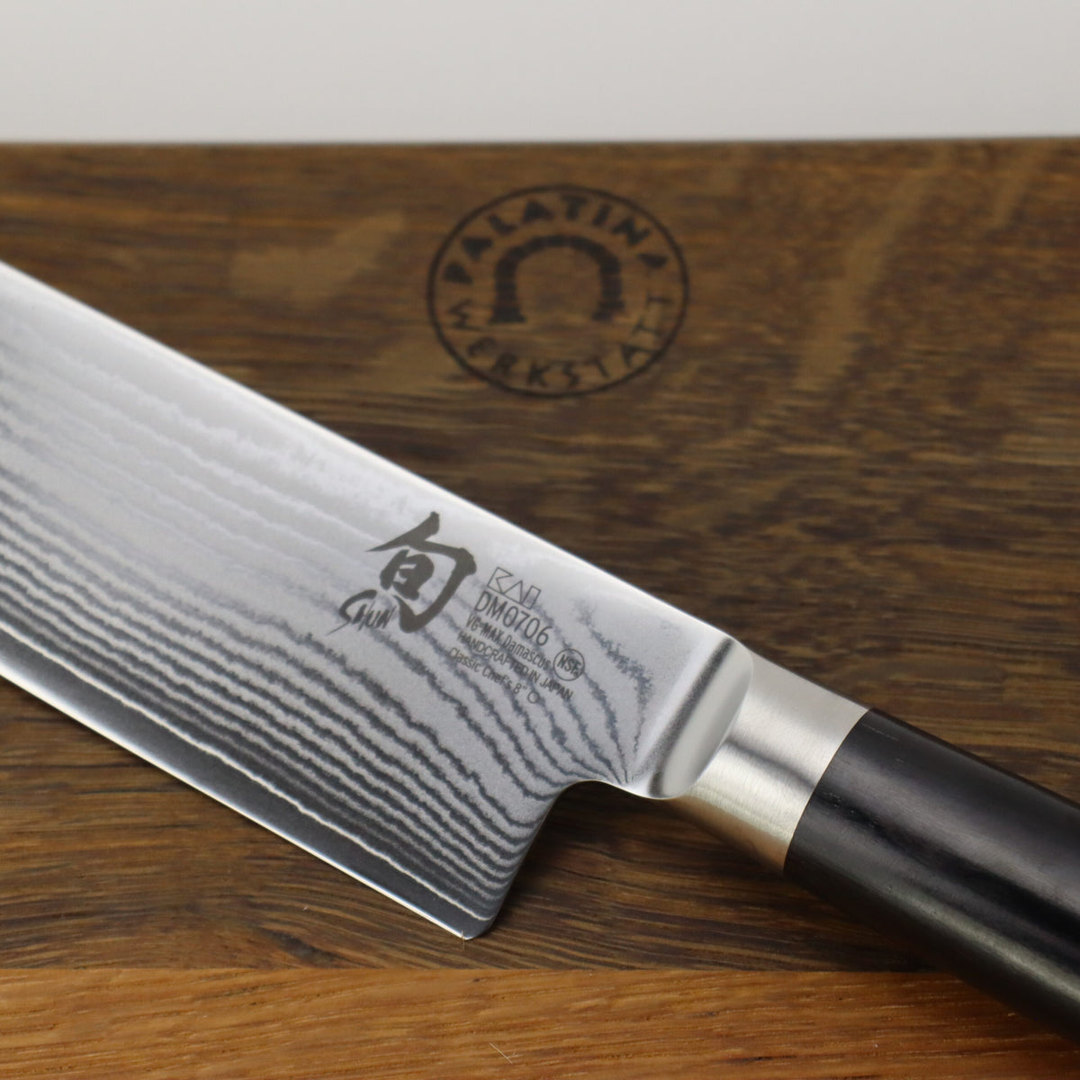 Eine Nahaufnahme eines hochwertigen Kai Shun Classic DM-0706 Kochmessers mit aufwendigen Klingenmustern und dunklem Griff, platziert auf einem XXL-Schneidebrett aus Fassholz (40x30 cm) mit eingraviertem Logo der „Pfälzer Werkstatt“. Die Klinge weist Kanji-Zeichen und den Markennamen „Kai Shun Classic“ auf.