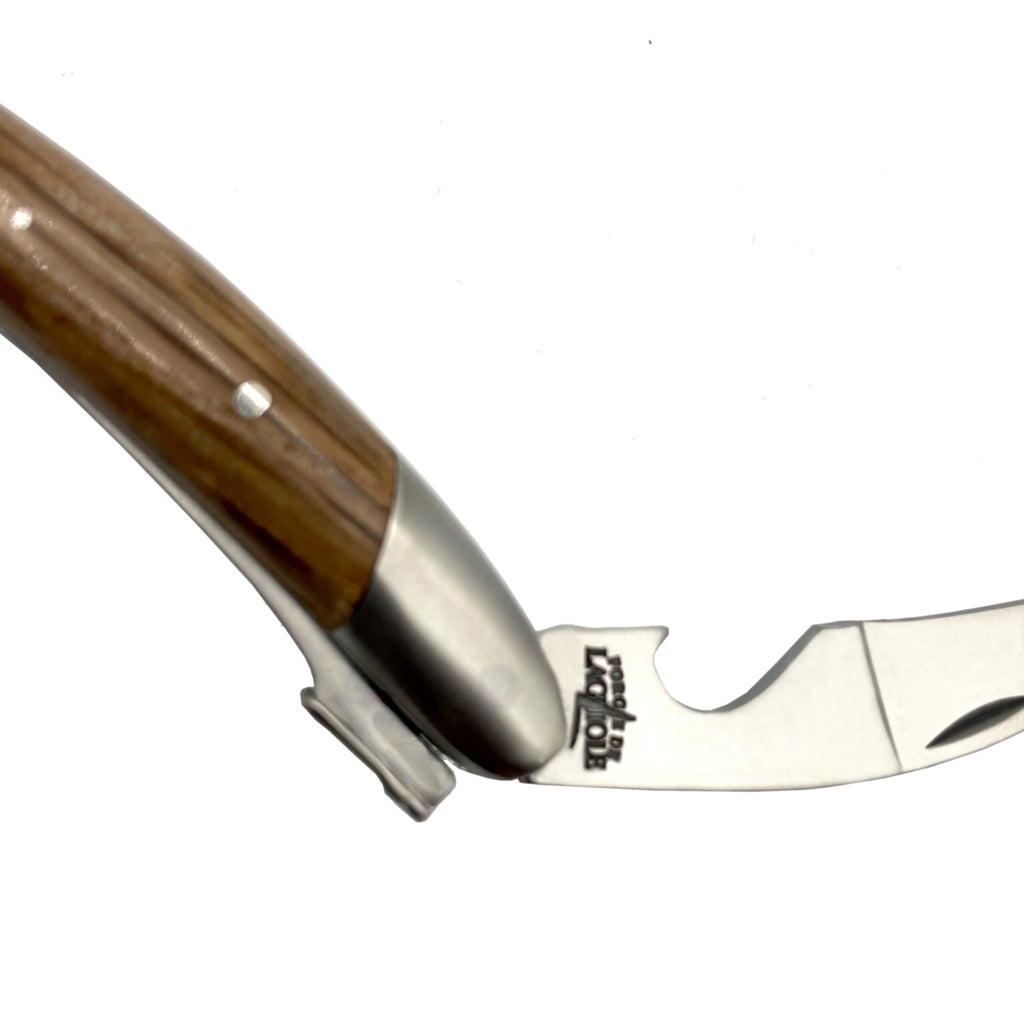 Eine Nahaufnahme des Forge De Laguiole Kellnermesser Sommelier | Mooreiche Rinde matt, ein Klapptaschenmesser mit Holzgriff. Die teilweise geöffnete Klinge verfügt über eine gezackte Kante und einen Flaschenöffner, der an den Forge De Laguiole-Stil erinnert. Das Markenlogo und der Text sind auf der Klinge in der Nähe des Scharniers sichtbar. Der Hintergrund ist weiß.