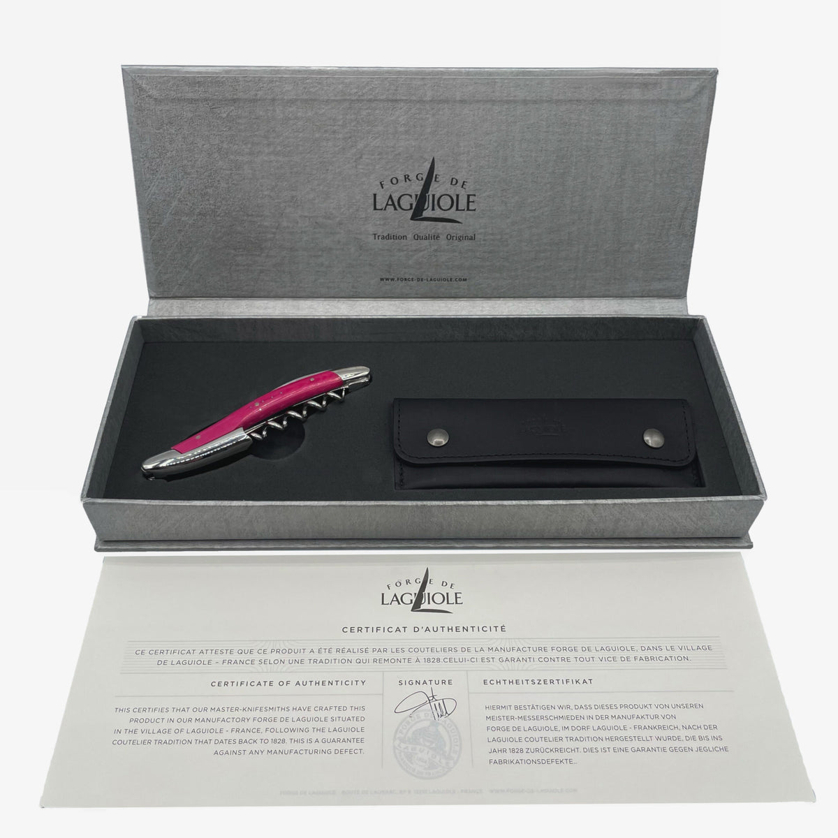 Ein hochwertiges Forge De Laguiole Kellnermesser Sommelier in rosa glänzend wird in einer offenen grauen Schachtel präsentiert, darunter befindet sich ein schwarzes Lederetui. Im unteren Teil des Bildes ist ein Echtheitszertifikat abgebildet, im Deckel der Schachtel sind das Logo und die Marke „Forge de Laguiole“ sichtbar.