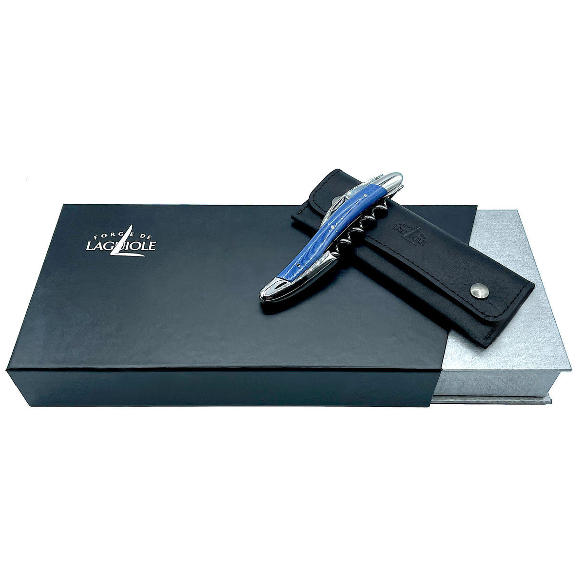 Ein elegantes „Forge De Laguiole Kellnermesser Sommelier | Blau glänzend“ ruht auf einem schwarzen Lederetui auf einer grauen Geschenkbox, die teilweise von einer größeren schwarzen Box mit silbernen Akzenten bedeckt ist. Die schwarze Box trägt das „Forge De Laguiole“-Logo in weißer Schrift.