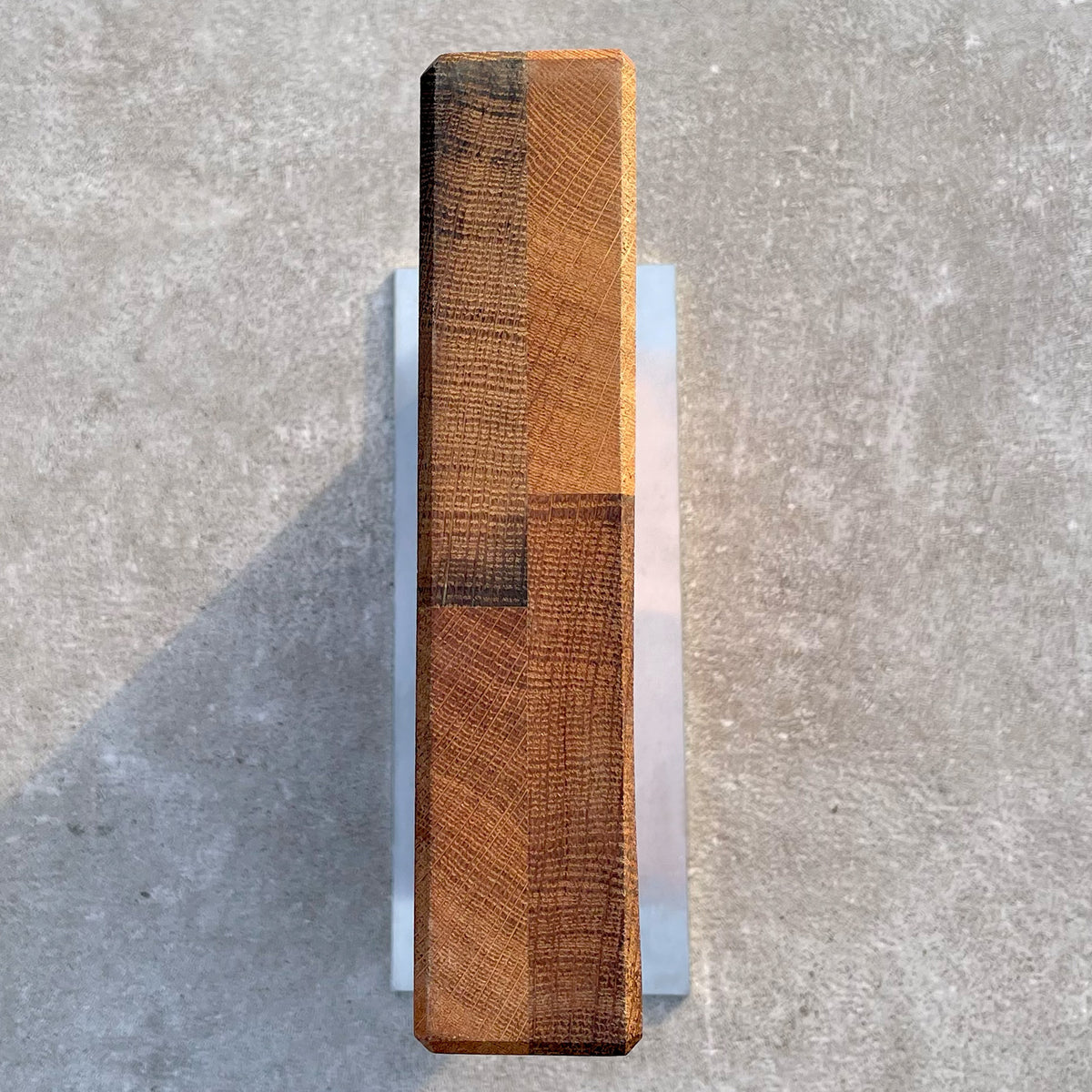Draufsicht des Palatina Werkstatt Magnet-Messerblocks mit Edelstahlsockel, gefertigt aus Fassdauben von alten Weinfässern, vertikal auf einer Betonoberfläche positioniert. Der Block hat eine glatte Oberfläche mit sichtbaren Holzmaserungen und unterschiedlichen Brauntönen. Der Schatten des Blocks erstreckt sich nach links auf den Beton.