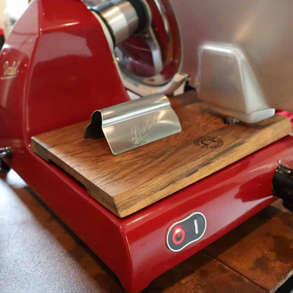 Auf einer Arbeitsplatte steht eine Berkel Original Aufschnittzange mit Holzsockel. Diese Aufschnittmaschine verfügt über einen silbernen Klingenschutz und einen Ein-/Ausschalter mit roter Kontrollleuchte.