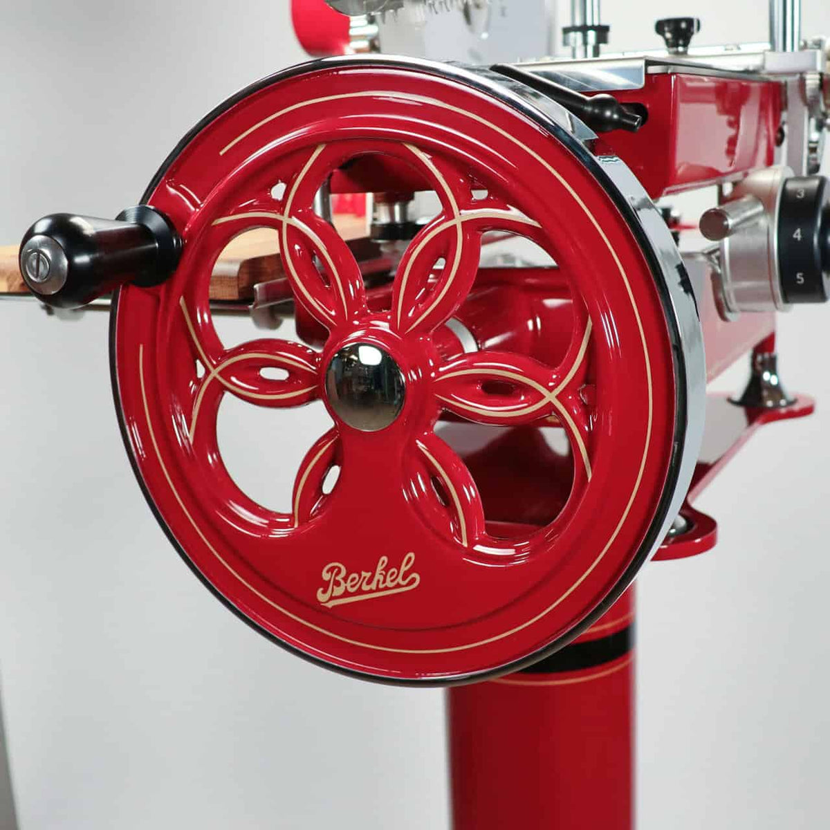 Nahaufnahme eines roten Handrads einer Berkel Volano B2 Schwungradmaschine im Vintage-Stil mit floralem Ausschnittdesign. Das Handrad zeigt unten in der Mitte deutlich das Berkel-Logo. Der Allesschneider hat eine glänzende Oberfläche mit Chromakzenten.