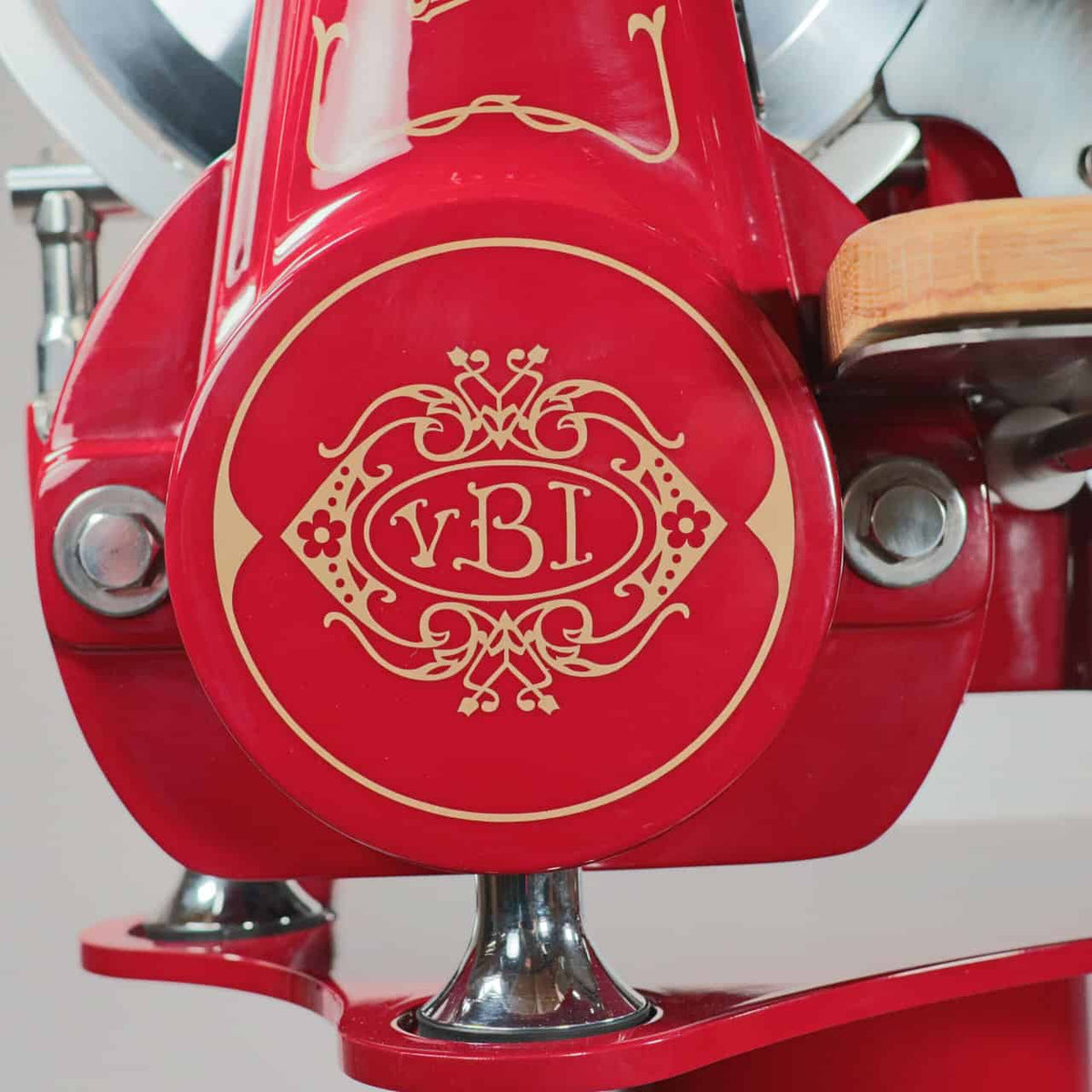 Nahaufnahme einer roten Vintage-Fleischschneidemaschine, der Berkel Volano B2 Schwungradmaschine in Rot, mit aufwendigen Goldmustern und dem Text „vB1“ in einem dekorativen Oval. Diese schöne Schneidemaschine verfügt über silberne Metallteile und einen Abschnitt einer Holzplattform.