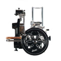 Vorderansicht des Berkel Volano B2 Schwarz, einer manuellen Schwungrad-Fleischschneidemaschine mit schwarzer und silberner Oberfläche. Die Maschine verfügt über eine große, runde schwarze Klingenabdeckung mit aufwendigen Mustern und wird mit einem Handkurbelmechanismus betrieben. Das Fassholz-Einlegebrett zum Halten des Fleisches befindet sich auf der linken Seite.
