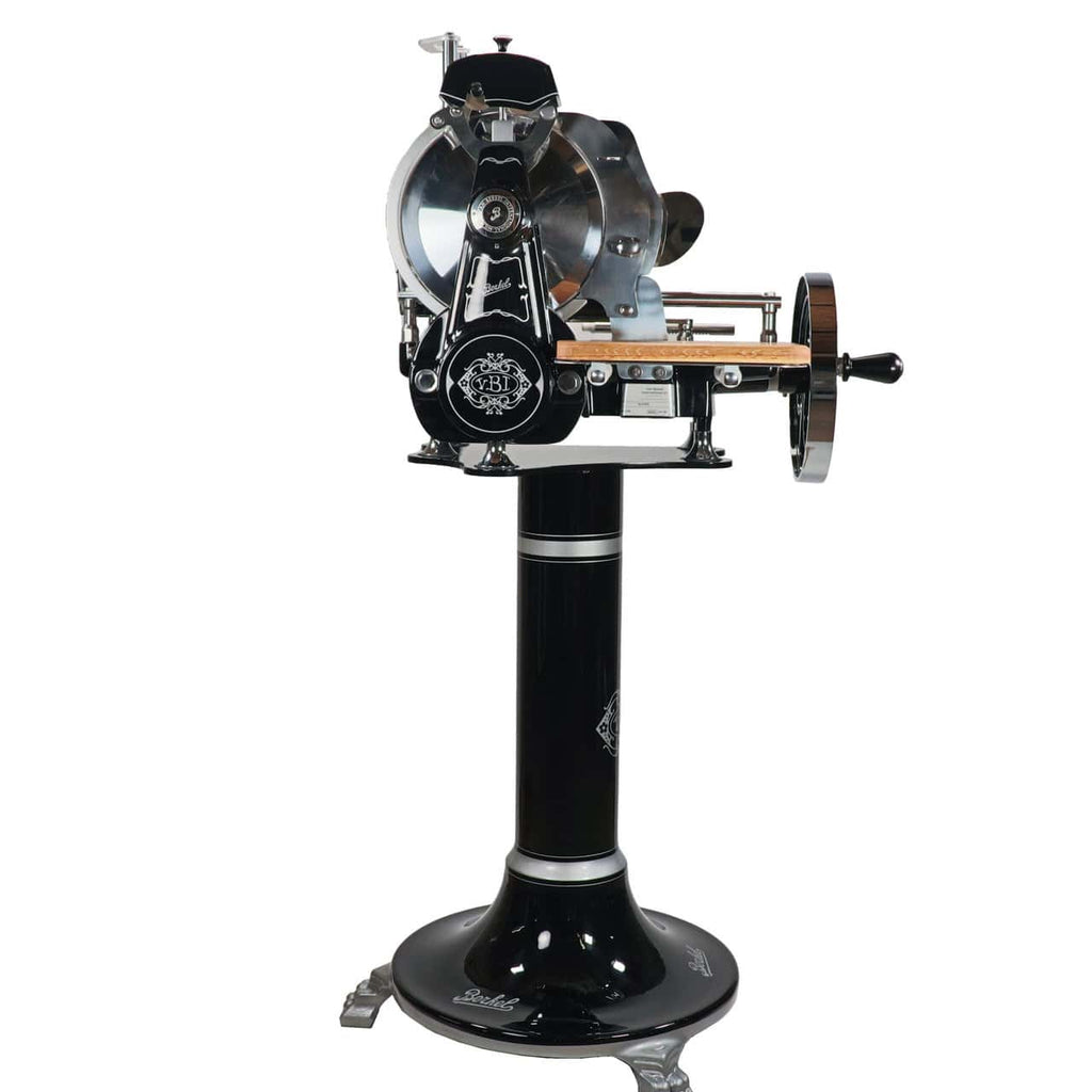 Eine wunderschöne, schwarze Berkel Volano B2 Schwungradmaschine mit Standfuß und einzigartigem Fassholzbrett Unikat. Diese charmante Aufschnittmaschine verfügt über eine Handkurbel und ein rundes Messer, mit kunstvollen Details und einem aufwendigen Design auf der Basis, das Funktionalität mit antikem Charme verbindet.