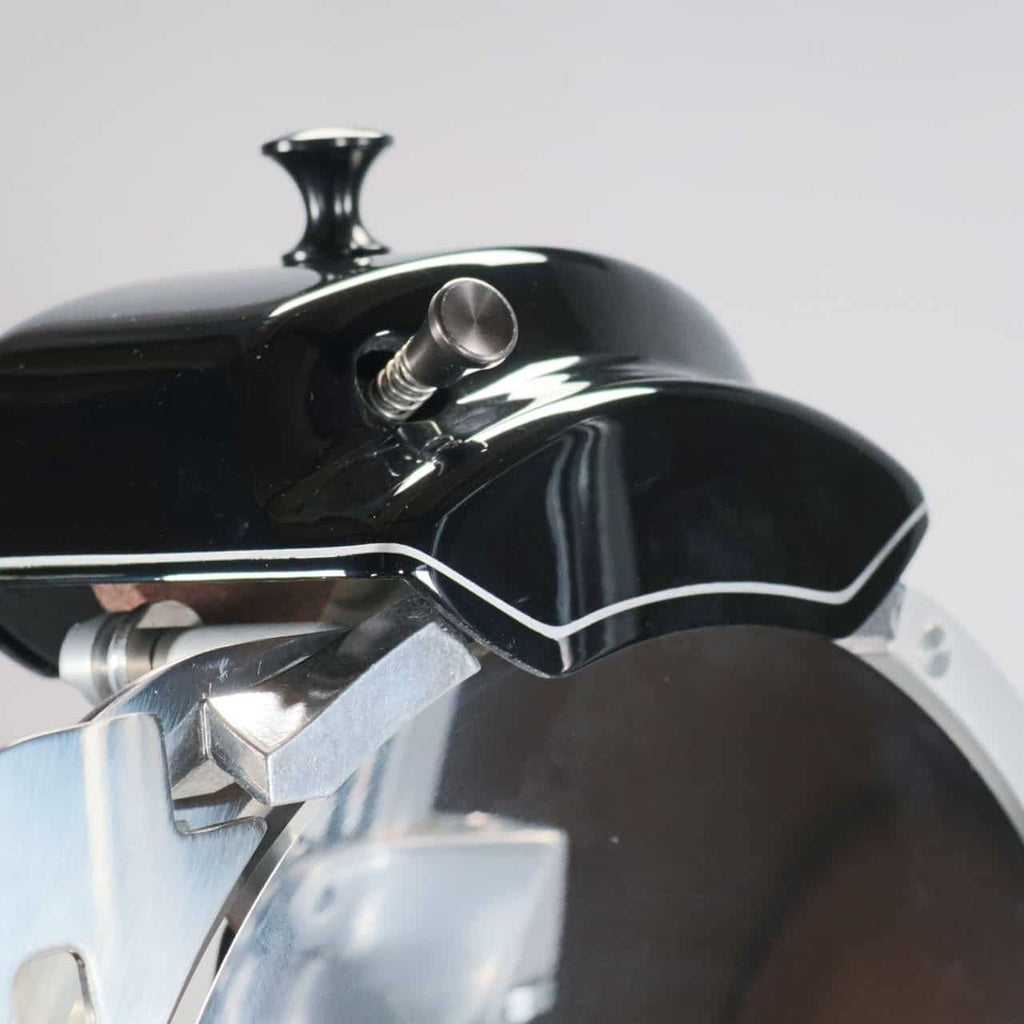 Nahaufnahme der Berkel Volano B2 Schwungradmaschine in Schwarz – ein schlanker, moderner schwarz-metallischer Handkurbelmechanismus mit glänzender Oberfläche und kleinem Hebel – möglicherweise Teil dieser wunderschön gestalteten Aufschnittmaschine mit Ständer und einzigartigem Fassholzbrett, vor einem neutralen Hintergrund.