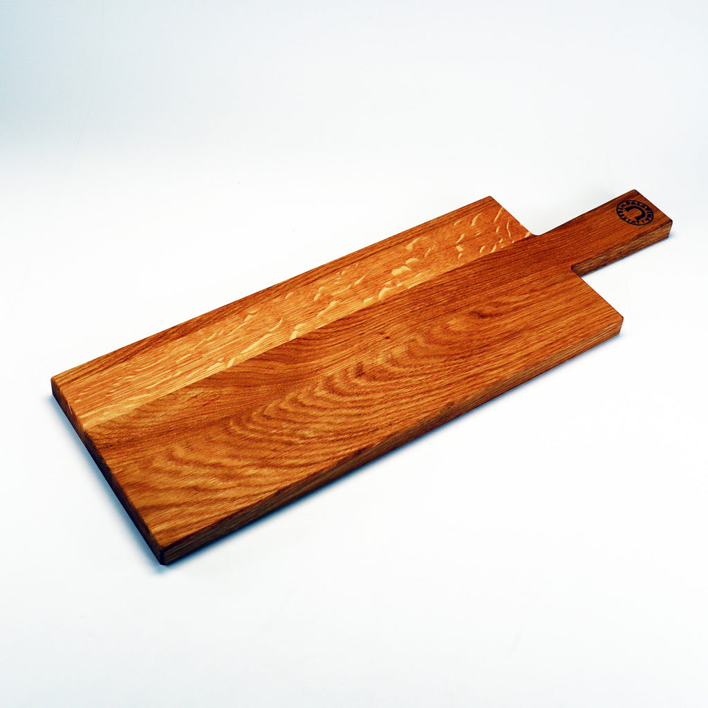 Ein rechteckiges Schneidebrett aus Holz, „Handgefertigtes Servierbrett für Wurst und Käse aus altem Weinfassholz“, hat einen Griff und eine glatte Oberfläche. Der Griff ist leicht vom Brett abgesetzt und in der Nähe seiner Unterseite befindet sich ein kleines geprägtes Emblem. Dieses handgefertigte Servierbrett verleiht jeder Küche Eleganz, wenn es vor einem schlichten weißen Hintergrund präsentiert wird.
