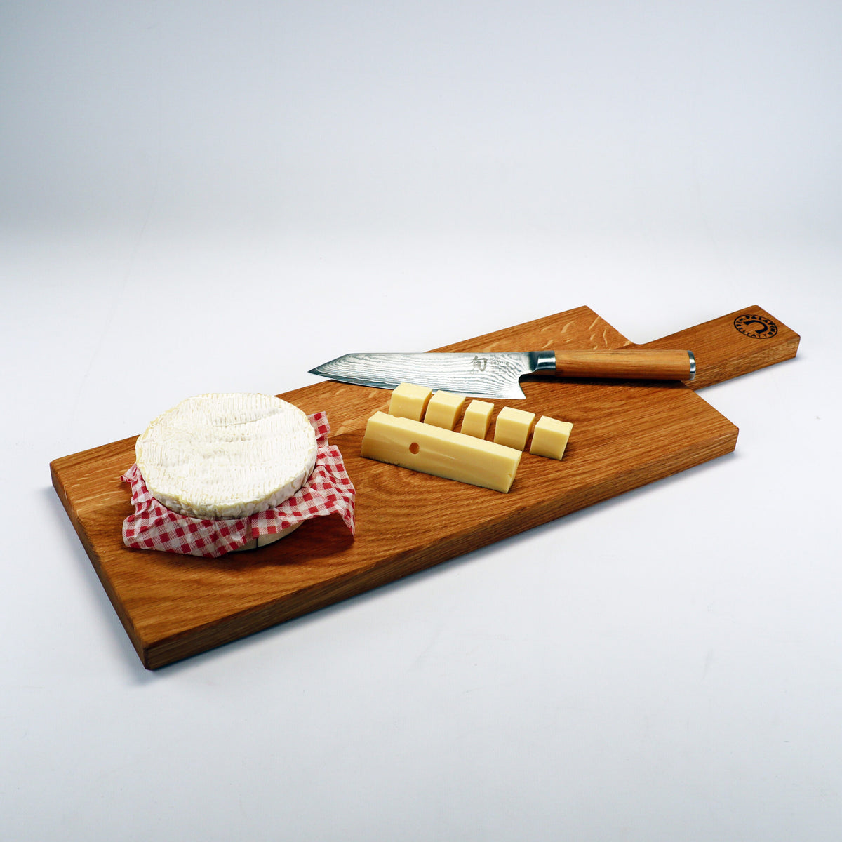Ein handgefertigtes Servierbrett für Wurst und Käse aus altem Weinfassholz mit einem Käsemesser, einer mit einem rot-weiß karierten Tuch bedeckten Käsescheibe und mehreren geschnittenen Käsestangen.