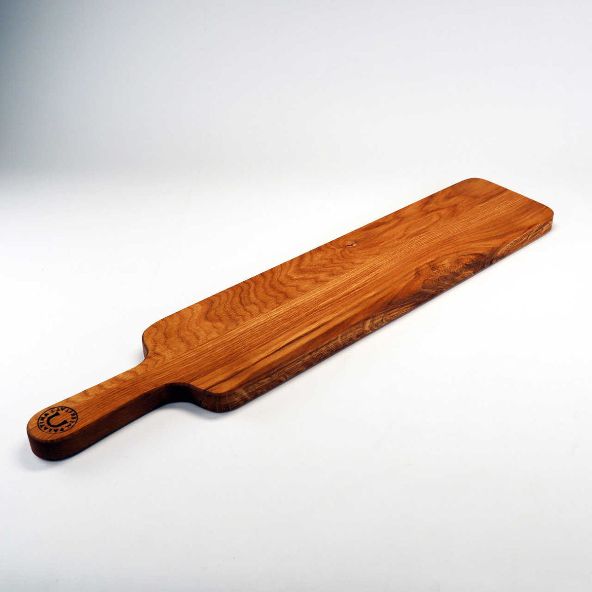 Ein langes, rechteckiges Servierbrett aus Holz von Palatina Werkstatt, gefertigt aus altem Weinfassholz und mit einem Griff an einem Ende sowie einer markanten Holzmaserung. Das handgefertigte Baguettebrett hat ein geprägtes Logo in der Nähe des Griffs und steht auf einem schlichten weißen Hintergrund.