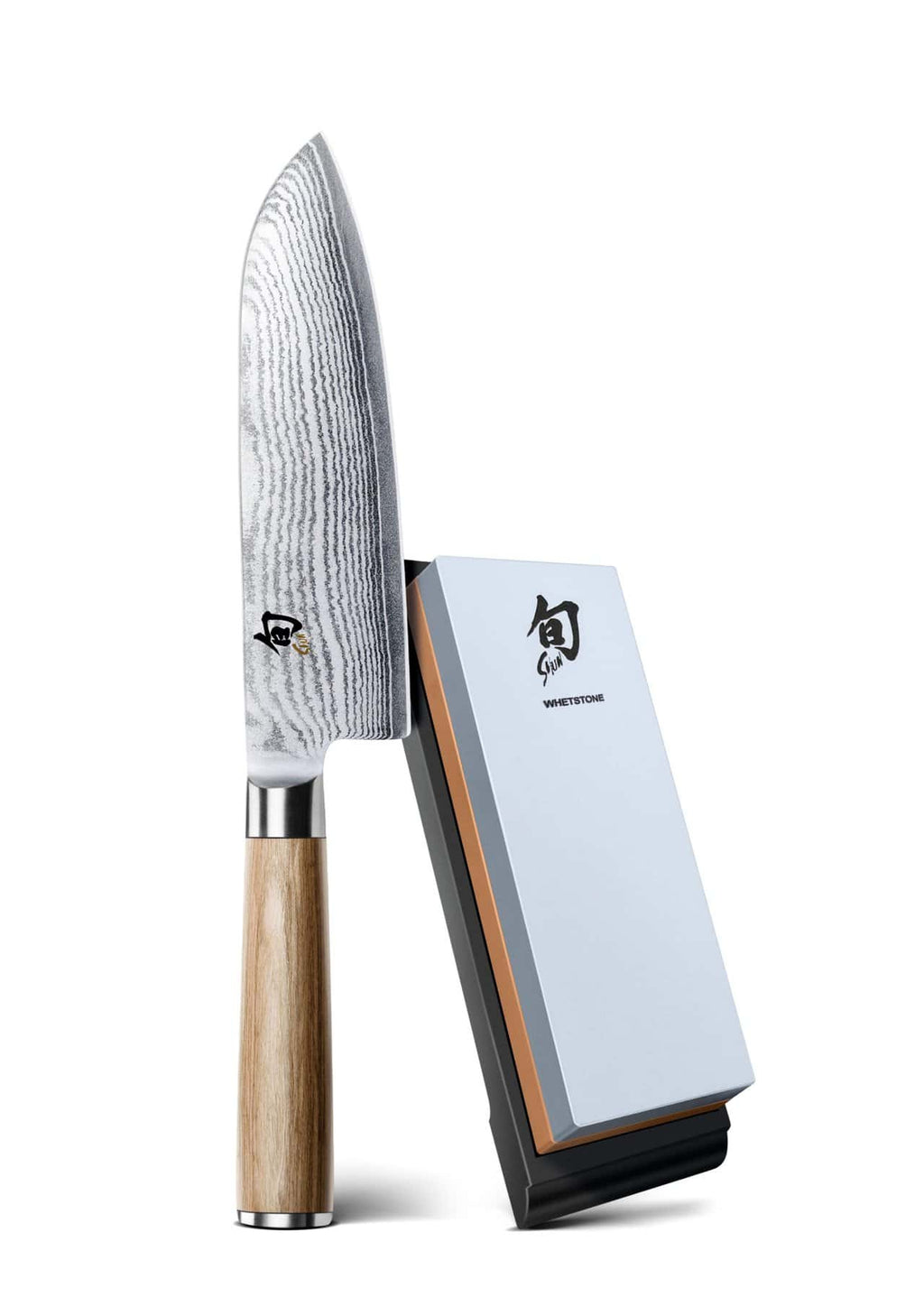 Das KAI X-MAS SELECTION DREAMBOX Shun Classic White Santoku mit einem unverwechselbaren Wellenmuster auf seiner Klinge aus Damaszenerstahl und einem Holzgriff wird elegant neben einem weiß-grauen Schleifstein präsentiert.