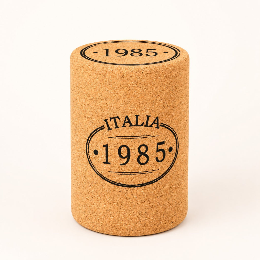 A Hochwertiger Hocker aus Kork in Stopfenform, mit "ITALIA 1985" vorne und "1985" oben, steht aufrecht vor weißem Hintergrund.