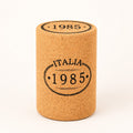 A Hochwertiger Hocker aus Kork in Stopfenform, mit "ITALIA 1985" vorne und "1985" oben, steht aufrecht vor weißem Hintergrund.