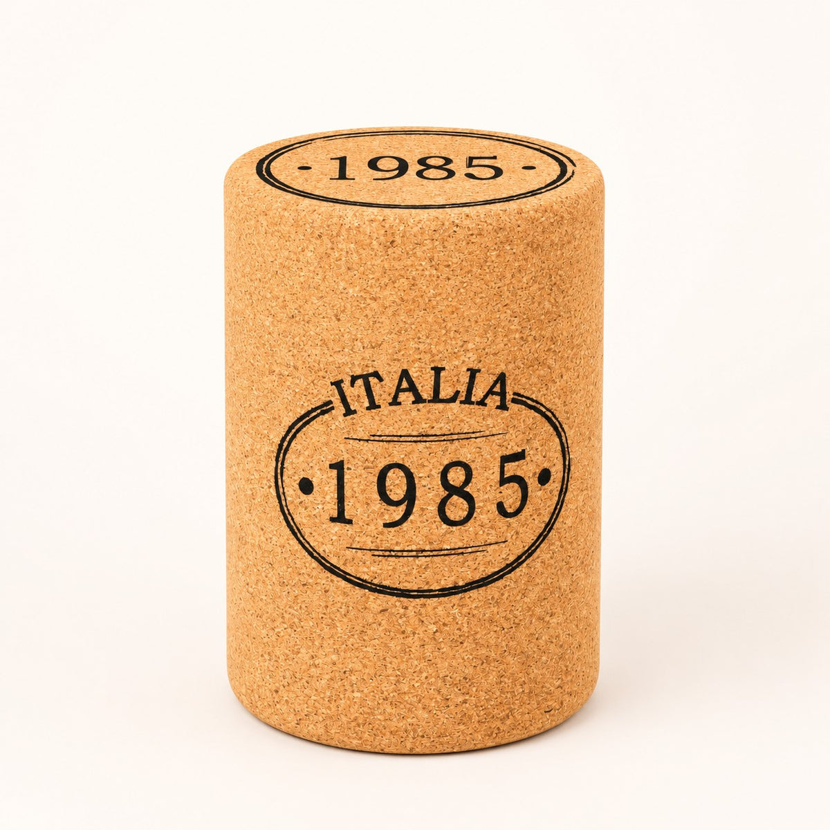 A Hochwertiger Hocker aus Kork in Stopfenform, mit "ITALIA 1985" vorne und "1985" oben, steht aufrecht vor weißem Hintergrund.