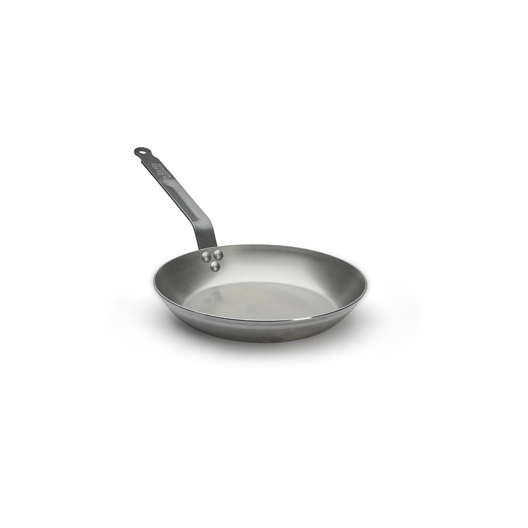 A De Buyer Lyonnaise Bratpfanne Carbone Plus mit langem Griff liegt auf einer weißen Fläche. Die hochwertige Bratpfanne aus Carbone Stahl ist leer und zeigt ihre glänzende, spiegelnde Oberfläche.