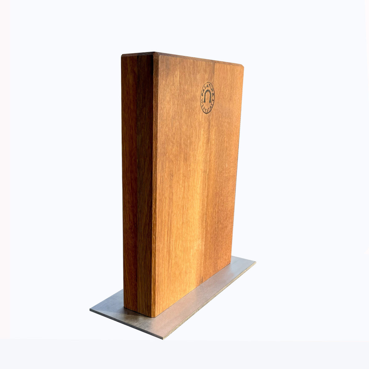 Ein Magnet-Messerblock von Palatina Werkstatt mit einem schlanken, minimalistischen Design sitzt auf einem Edelstahlsockel. Das Holz, recycelt aus alten Weinfässern, hat ein natürliches Finish mit einem feinen Maserungsmuster. Ein kleines, kreisförmiges Logo ist in die obere linke Ecke des Blocks eingraviert. Der Hintergrund ist reinweiß.