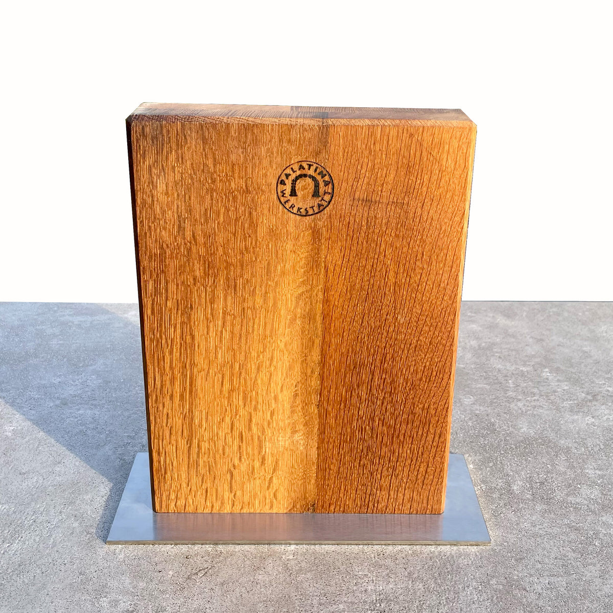Ein Magnet-Messerblock mit Edelstahlsockel aus Fassdauben von alten Weinfässern, mit glatter Oberfläche und einem Logo der Palatina Werkstatt auf der Vorderseite. Der Block steht auf einem Edelstahlsockel, vor einem schlichten, hellen Hintergrund.