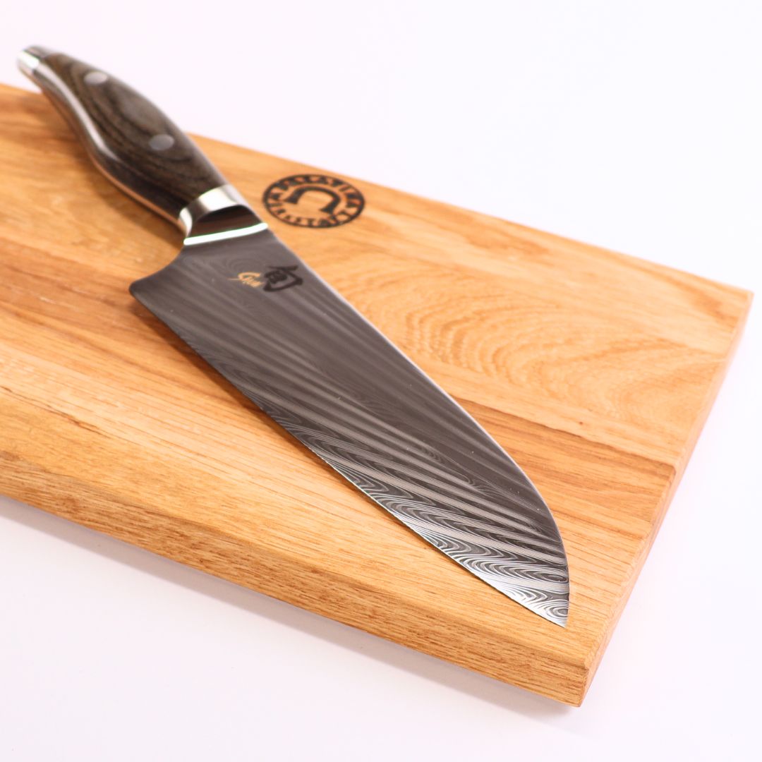 Das Kai Shun Nagare NDC-0706 Kochmesser (72 Lagen Damast, 20 cm) mit gemusterter Klinge und dunklem Griff liegt auf einem 30x20 cm basaltgrauen Schneidebrett aus Eiche.
