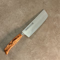 Ein Nakiri-Küchenmesser aus der Palatina Werkstatt Messerserie mit einer 16 cm langen polierten Edelstahlklinge und einem aufwendig gemusterten Olivenholzgriff liegt auf einer strukturierten, hellbraunen Oberfläche. Der Markenname „PALATINA Werkstatt Wagyu Style“ ist in die Klinge eingraviert.