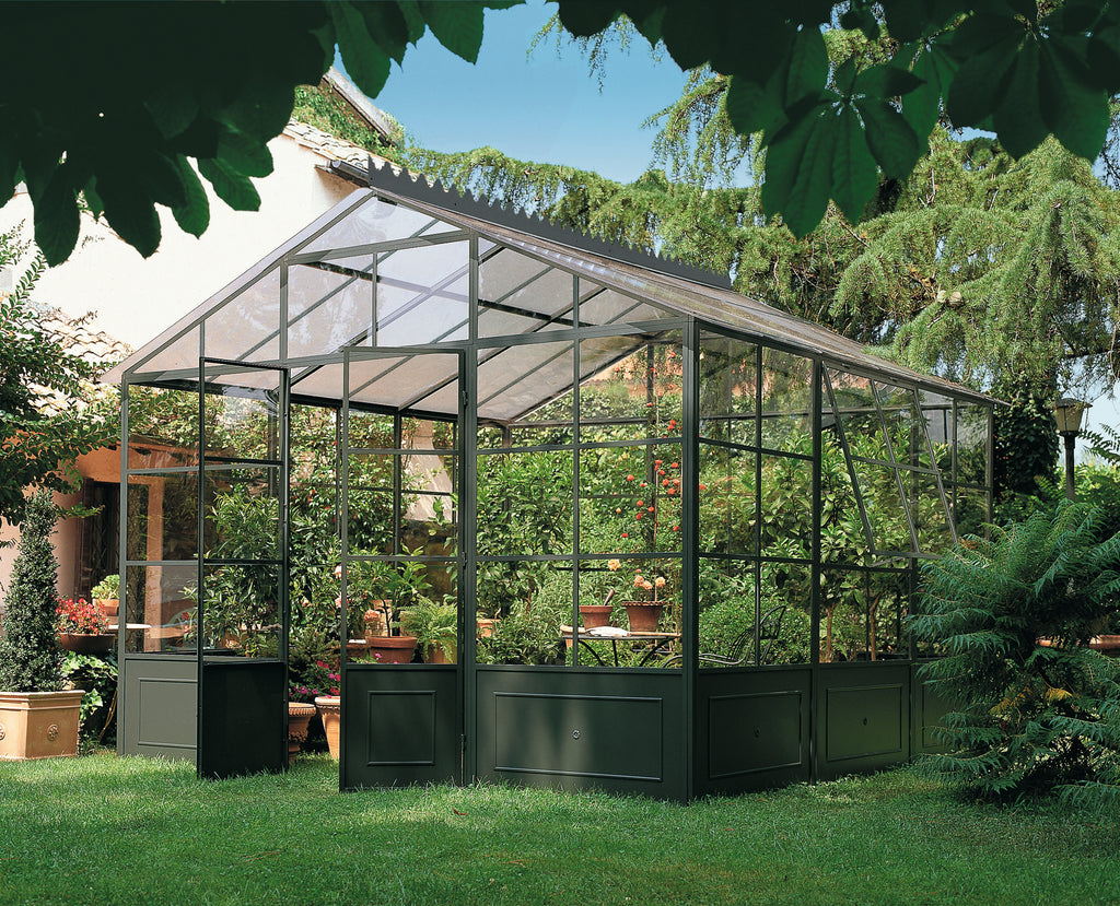 Ein üppiger grüner Garten mit einer freistehenden Orangerie aus Glas, die mit verschiedenen Topfpflanzen und Blumen gefüllt ist. Die Orangerie hat einen Metallrahmen und ist von hohen Bäumen und lebendigem Grün umgeben. Sonnenlicht fällt durch die Blätter und erzeugt eine ruhige, natürliche Atmosphäre.