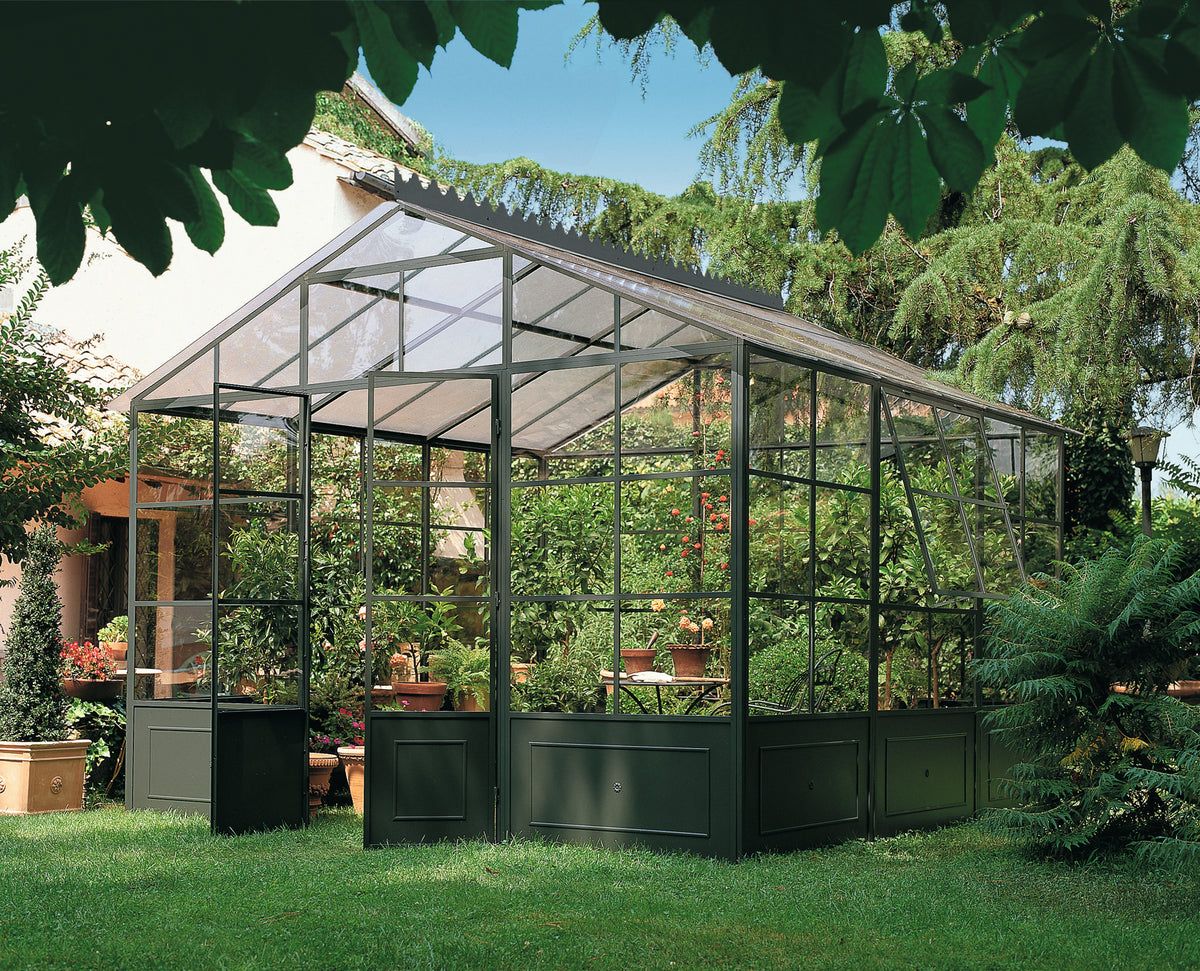 Ein üppiger grüner Garten mit einer freistehenden Orangerie aus Glas, die mit verschiedenen Topfpflanzen und Blumen gefüllt ist. Die Orangerie hat einen Metallrahmen und ist von hohen Bäumen und lebendigem Grün umgeben. Sonnenlicht fällt durch die Blätter und erzeugt eine ruhige, natürliche Atmosphäre.