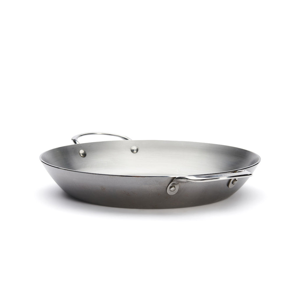 A De Buyer Paella-Pfanne Mineral B, 32 cm Durchmesser, aus Stahl mit einem langen und einem kurzen Griff steht auf weißem Hintergrund.
