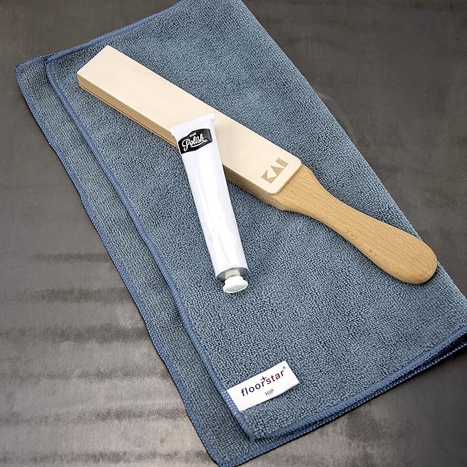 Ein Set mit Schuhpflegewerkzeugen auf einer flachen Oberfläche umfasst ein graues Mikrofasertuch, eine hölzerne Schuhbürste mit flachem Kopf und Griff sowie eine Tube weiße Schuhcreme. Das Tuch hat ein Etikett mit der Aufschrift „floor☆star“, und das Kai Shun Polierriemen-Set mit Abziehriemen vervollständigt dieses Premium-Set für die perfekte Schuhpflege.