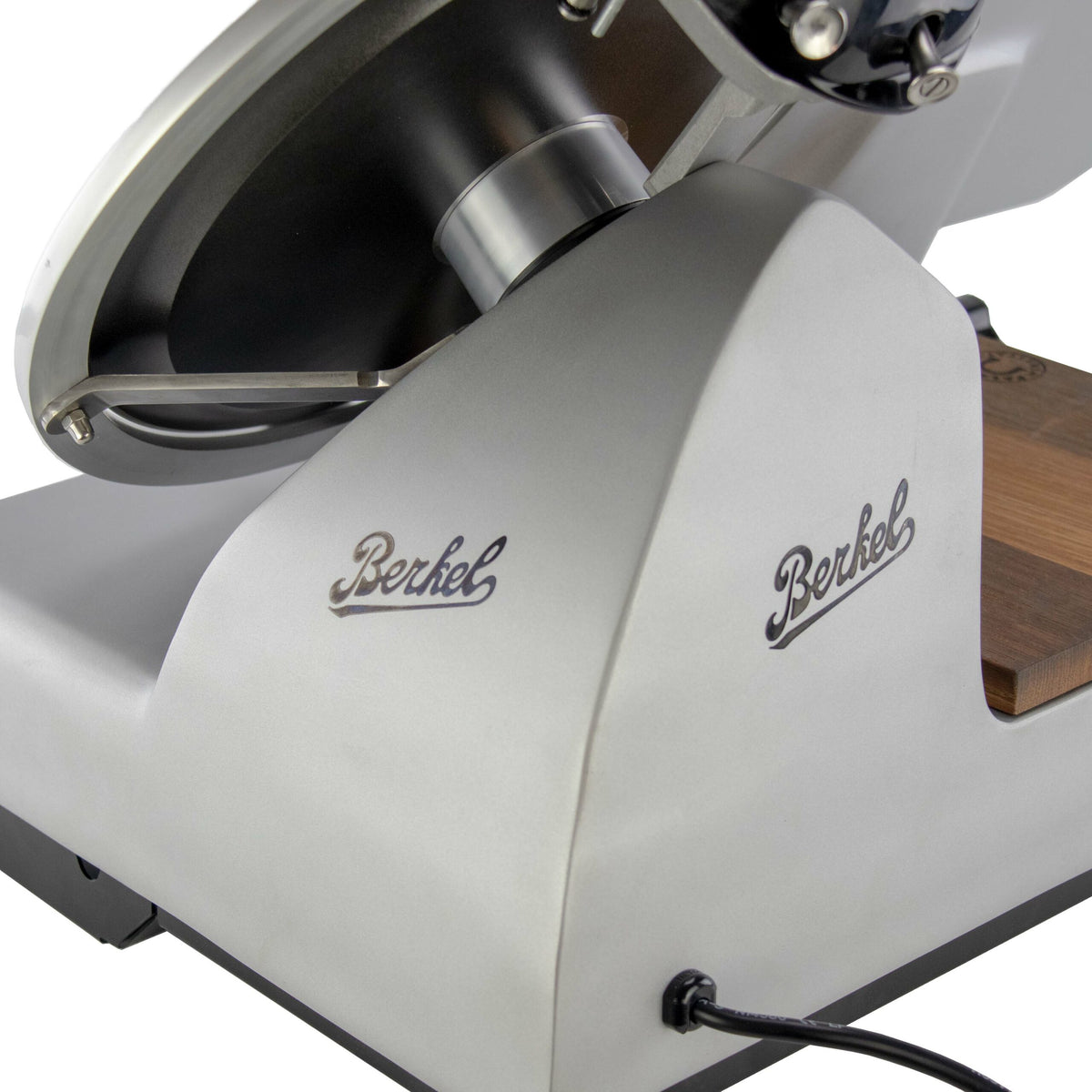 Eine Nahaufnahme einer Berkel Red Line Weis-Fleischschneidemaschine, Modell 300 mm Original Profi-Aufschnittmaschine + Weinfass Einlegebrett, zeigt das robuste Metallgehäuse der Maschine mit der Aufschrift „Berkel“ auf jeder sichtbaren Seite. Die Klinge der Profi-Aufschnittmaschine und ein Teil ihres Holzsockels sind ebenfalls teilweise sichtbar.
