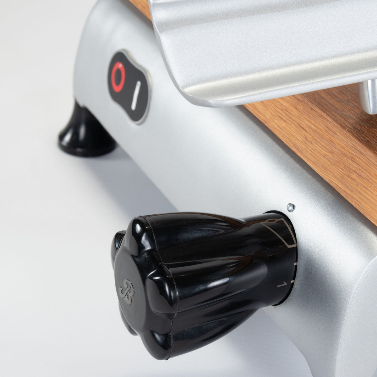 Nahaufnahme eines schwarzen Knopfs auf einem eleganten Berkel Red Line 250 Grau Teflon-Küchengerät mit silbernem und hölzernem Design. Der Knopf hat ein sternförmiges Muster auf seiner Oberfläche und oben im Bild ist ein Netzschalter mit Ein- und Aus-Positionen zu sehen.