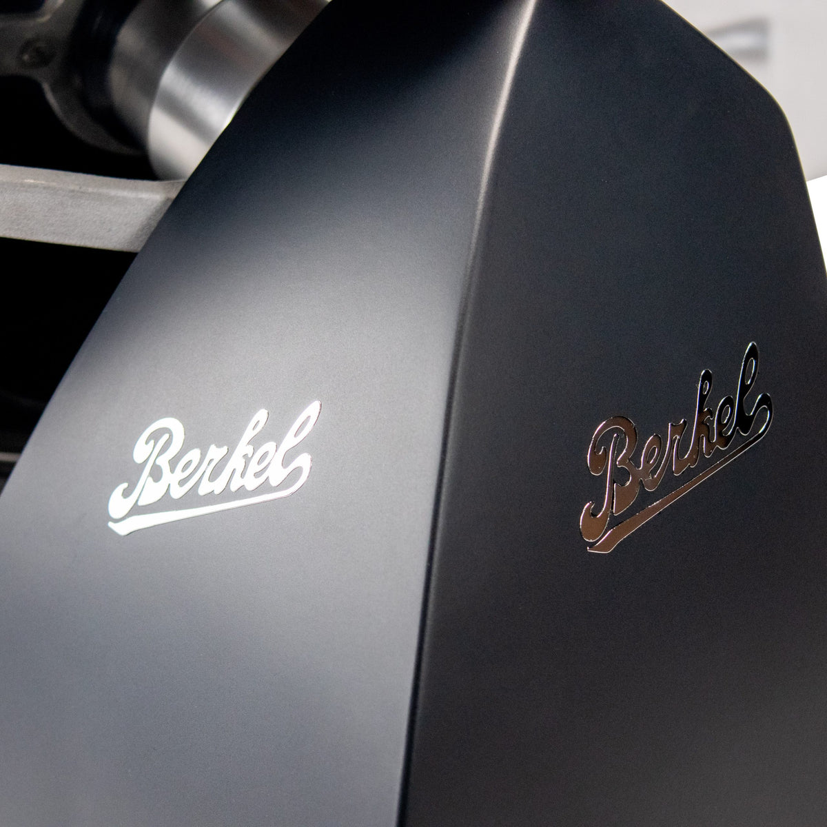 Eine Nahaufnahme des Berkel RedLine 250 MATT in Schwarz mit Fassholzbrett zeigt sein schlankes, modernes Design. Der Name „Berkel“ ist stilvoll zweimal in metallischer Schrift eingraviert und unterstreicht seine glänzende Attraktivität und den prestigeträchtigen Markennamen.