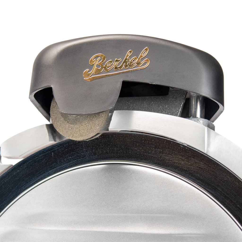 Nahaufnahme des Klingenschärfers einer Fleischschneidemaschine vom Typ Berkel RedLine 250 MATT rot. Das elegante Metalldesign wird zur Schau gestellt und das Berkel-Logo ist deutlich in goldener Schrift zu sehen.