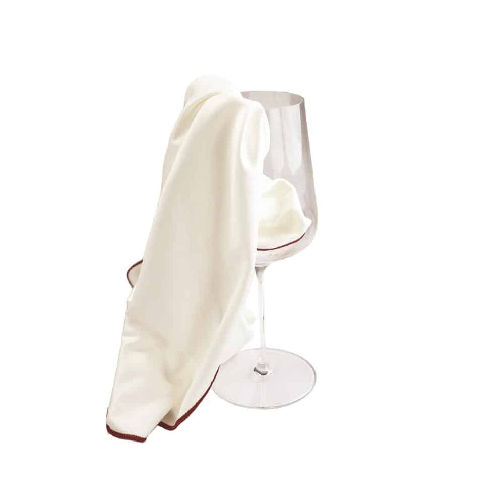 Ein weißes Tuch mit kastanienbraunem Rand, das an ein Mikrofasertuch erinnert, ist vor einem schlichten weißen Hintergrund elegant über den Rand eines leeren, klaren Riedel-Weinglases drapiert.